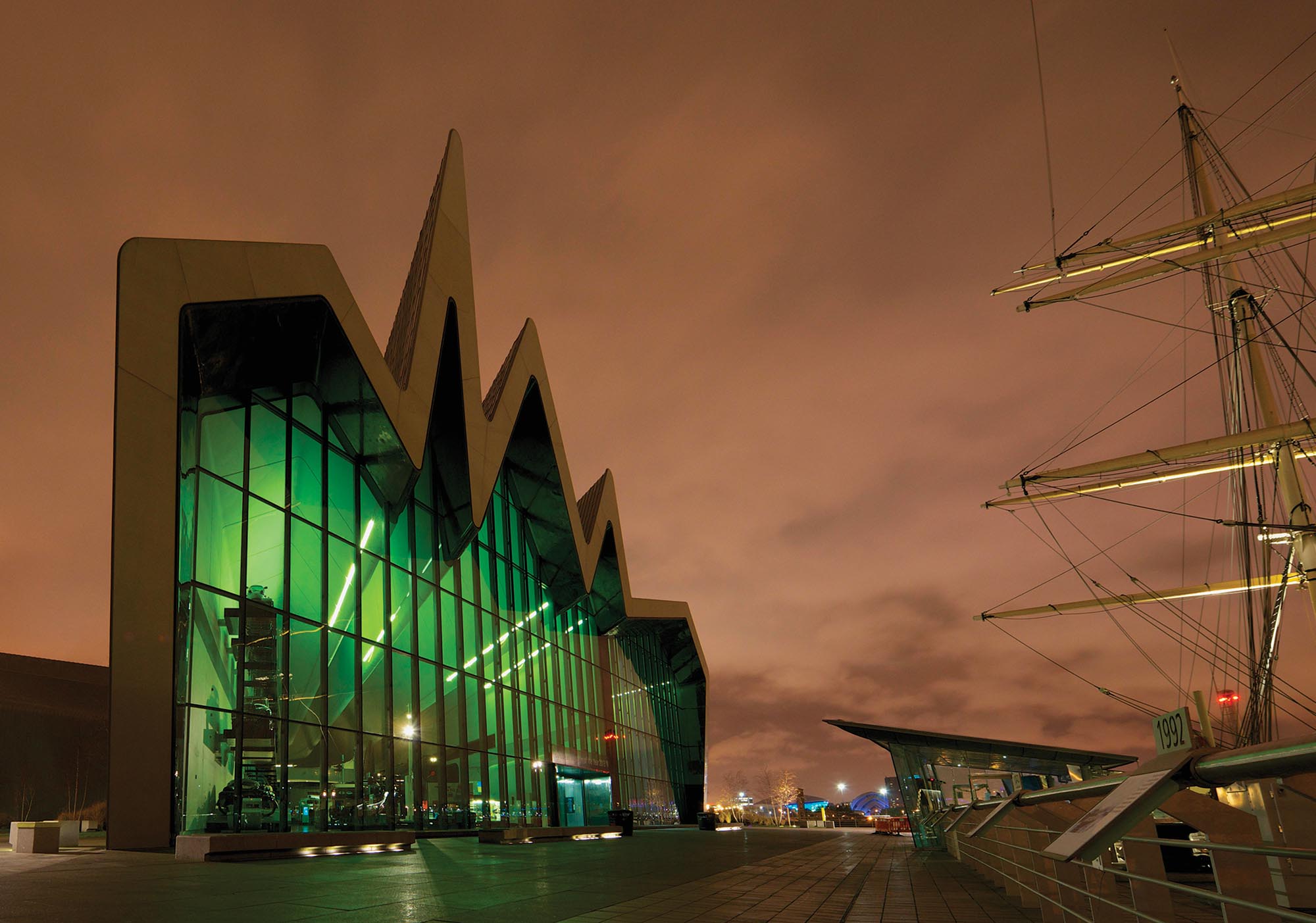 A museum with a floor to ceiling wall of glass. The roof is in the shape of a jagged wave.