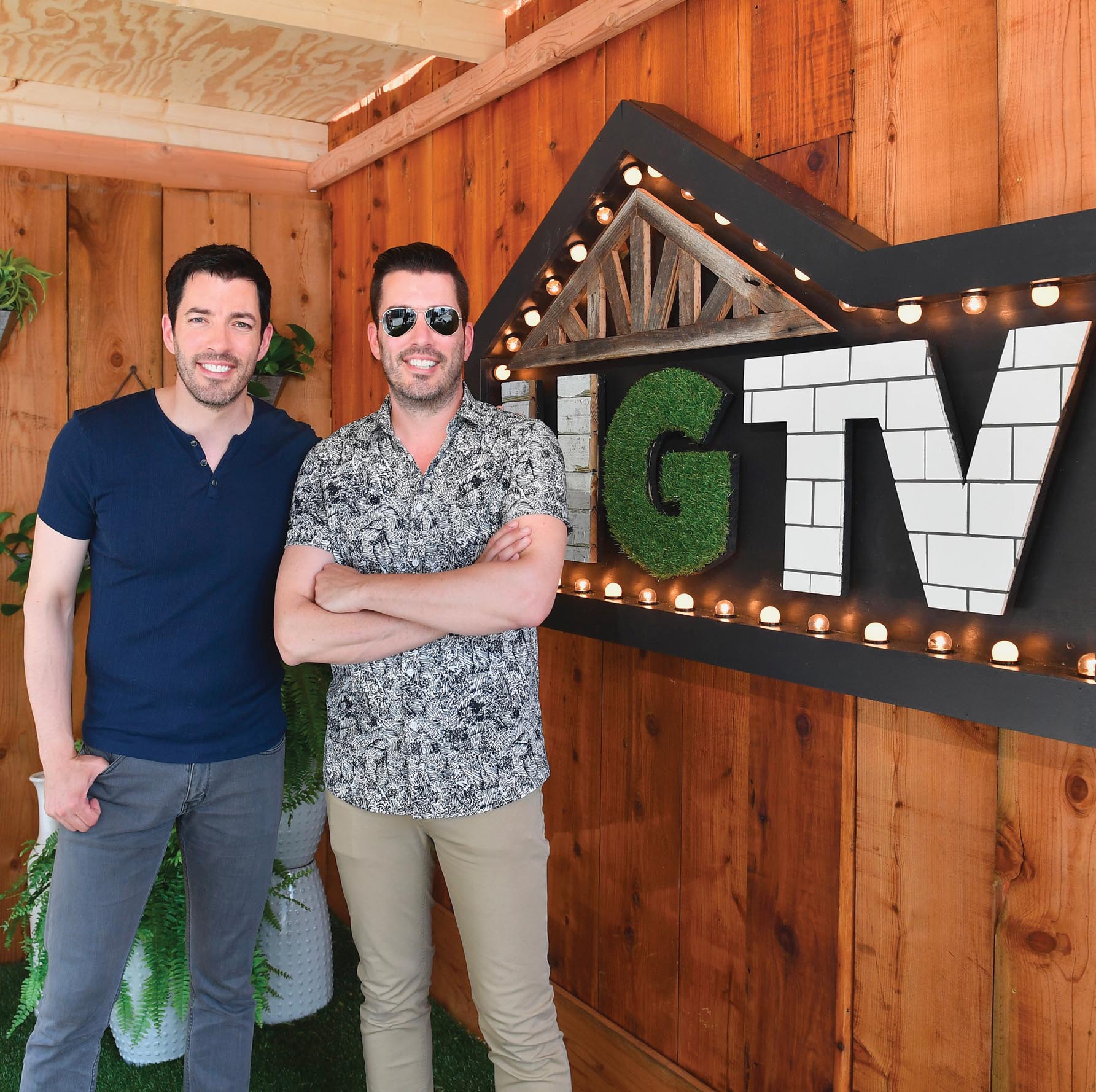 The Property Brothers pose for a picture in front of an H G T V sign.