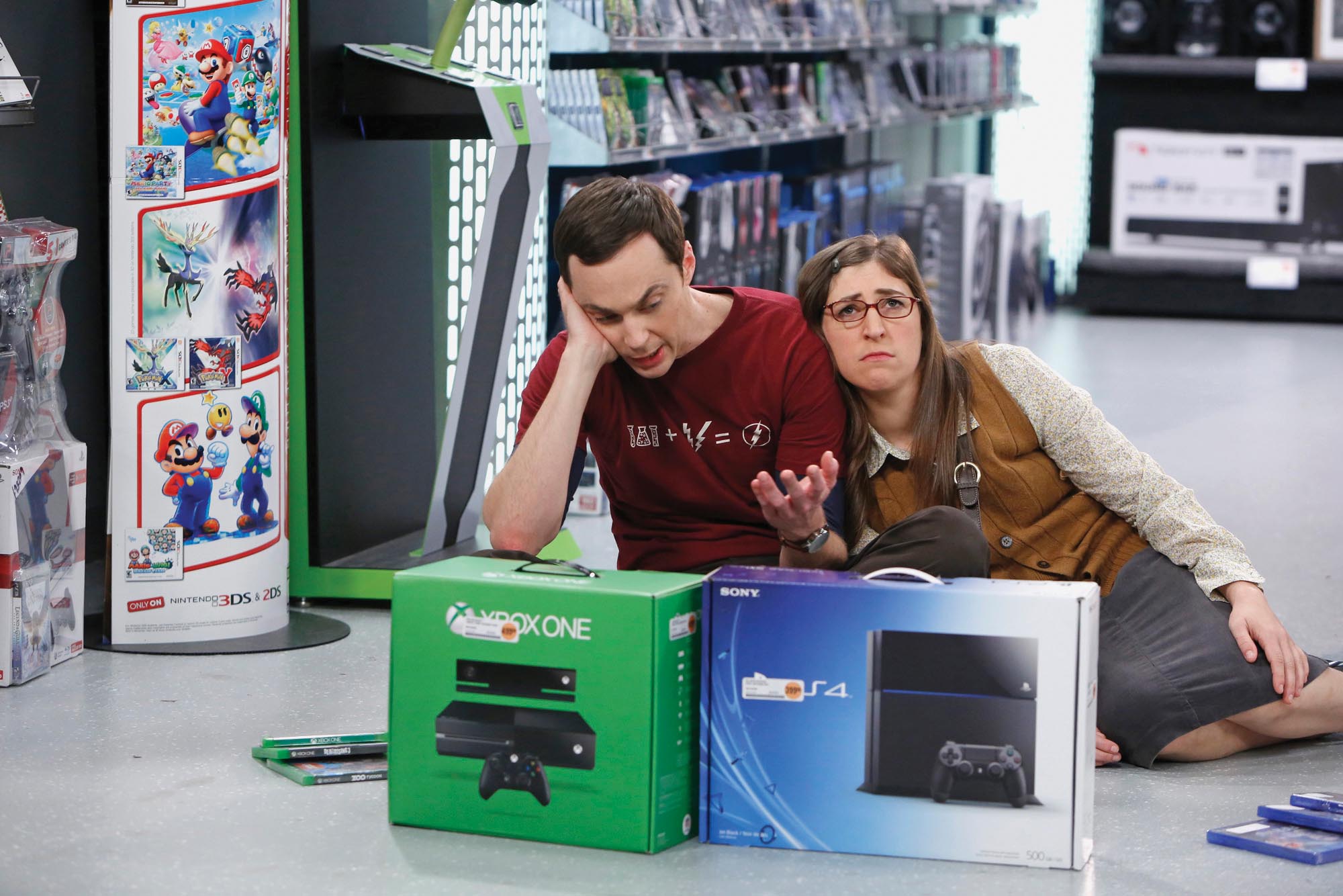 Amy rolls her eyes in despair as Sheldon deliberates between an Xbox and a PlayStation.