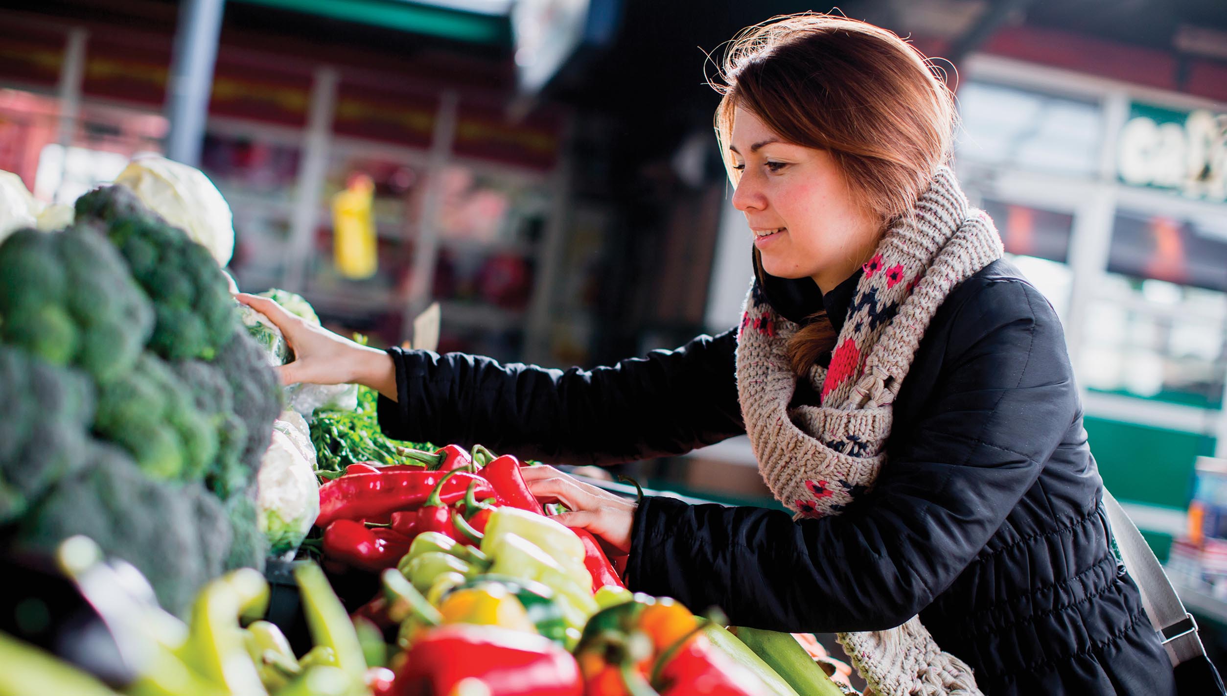 A person choosing vegetables from a table of produce at an outdoor market.