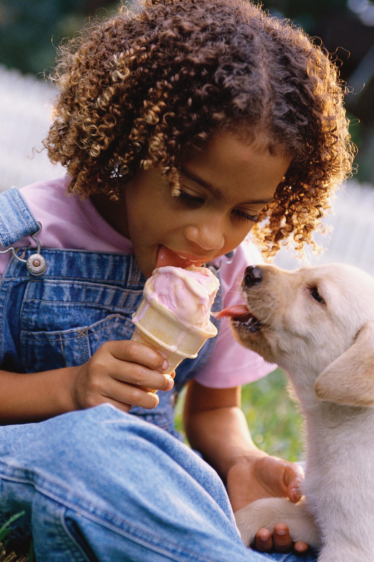 A little girl is sitting down and eating an ice-cream cone.