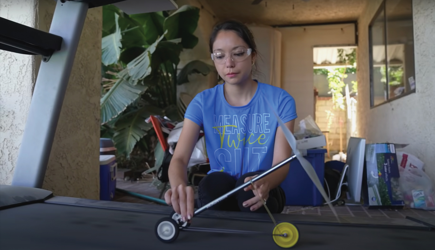 YouTuber Xyla Foxlin places a wind-powered model vehicle on an exercise treadmill and observes the model’s performance.