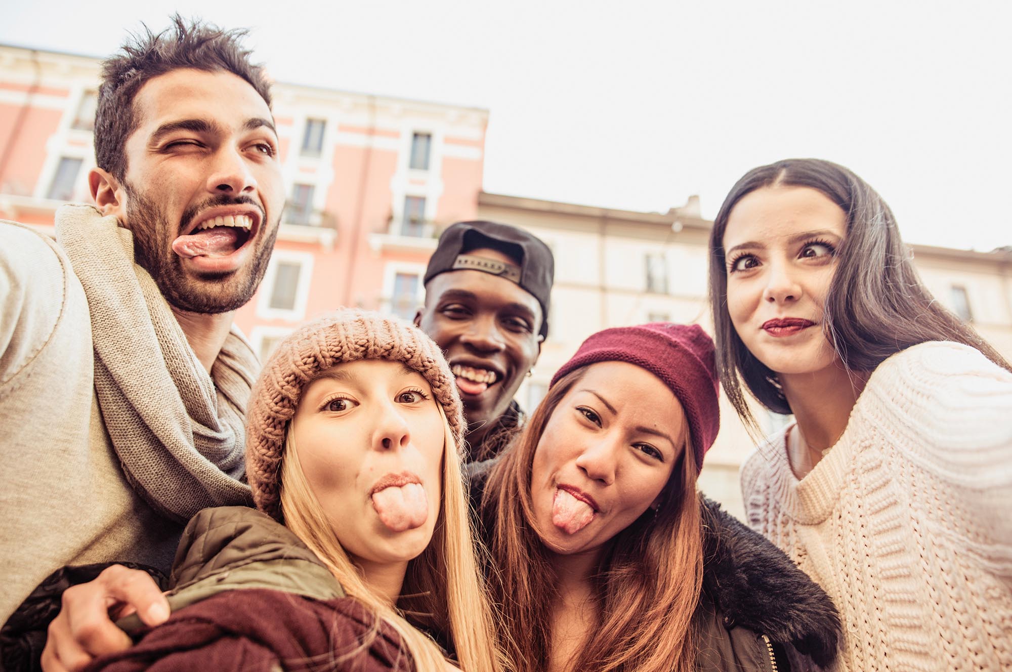 A group of 5 people taking a selfie while making silly faces and sticking out their tongues.