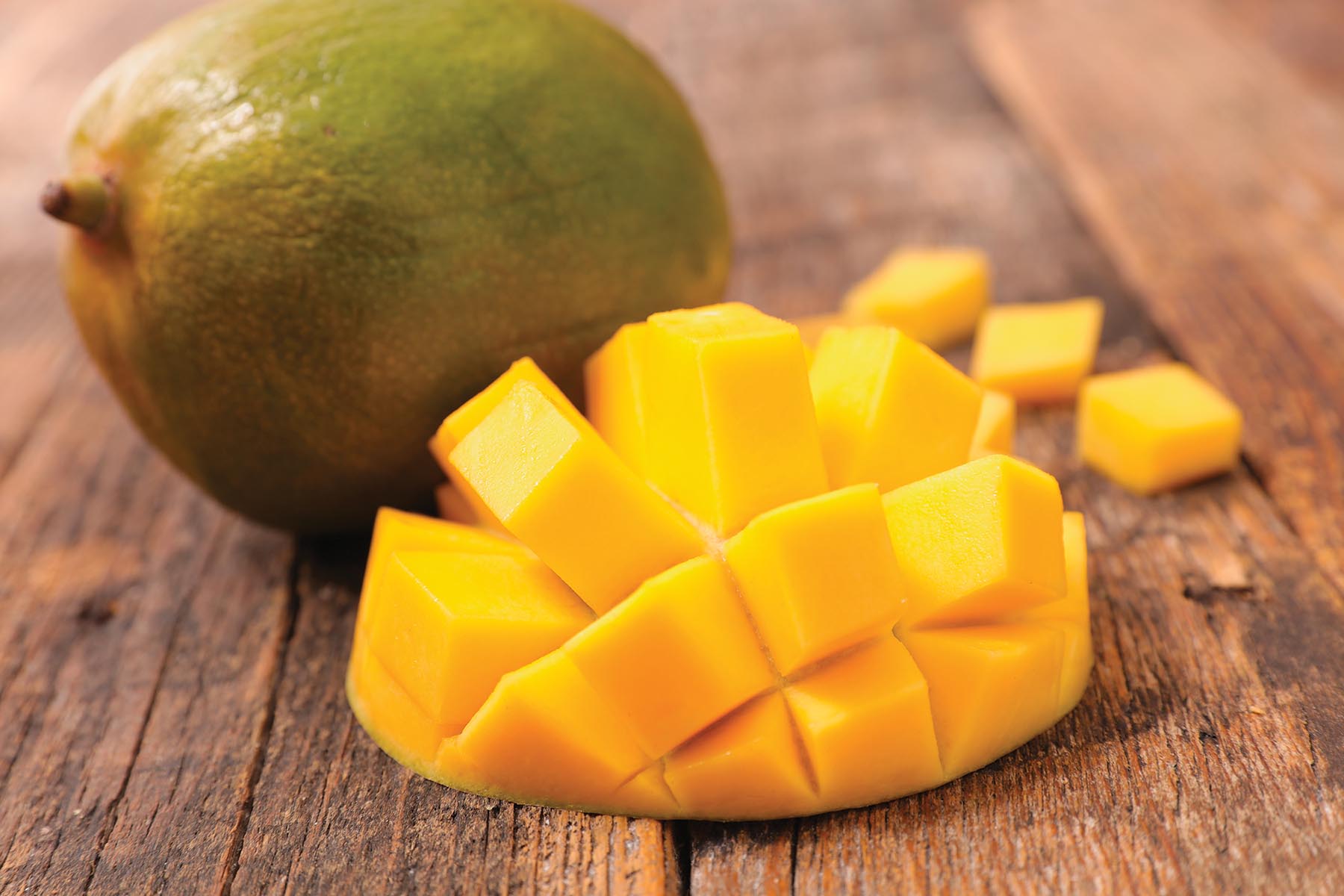 A whole mango next to one that has been peeled and cut into cubes.