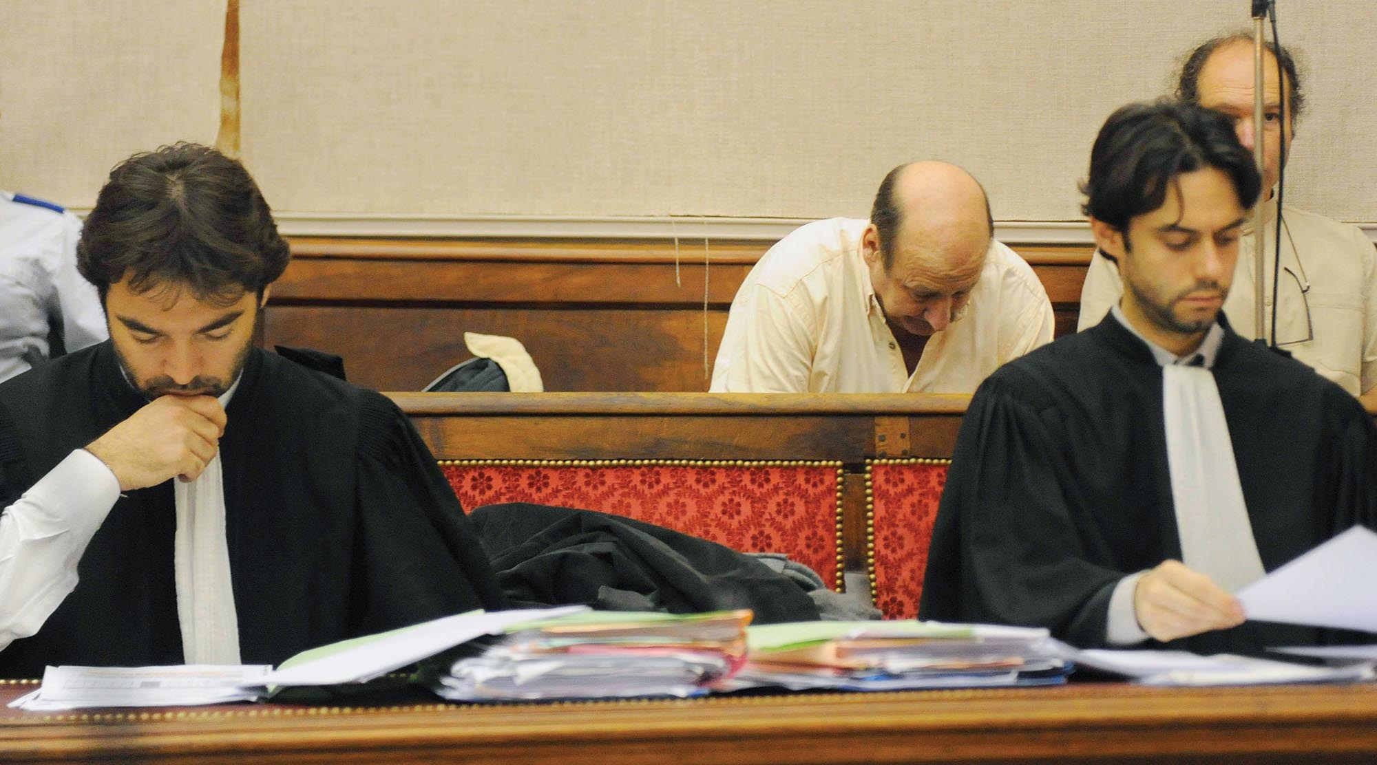 Two European lawyers in robes sit at a courtroom table.