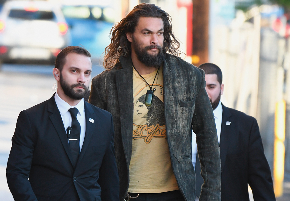 Jason Momoa flanked by two bodyguards.; Amy rolls her eyes in despair as Sheldon deliberates between an Xbox and a PlayStation.