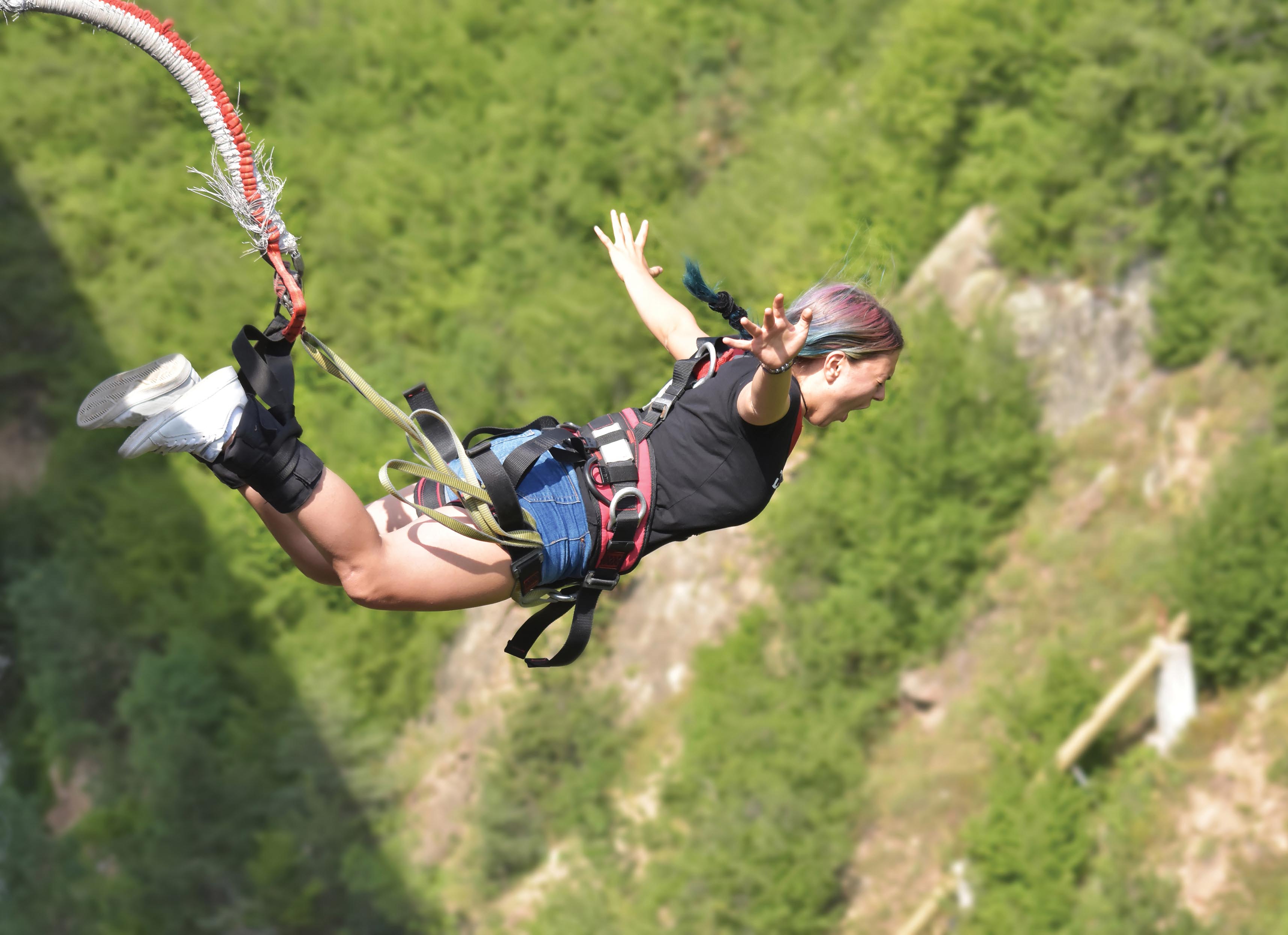 A photo of a woman doing Bungee jumping. Her arms are stretched wide and screams as she flies in the air.