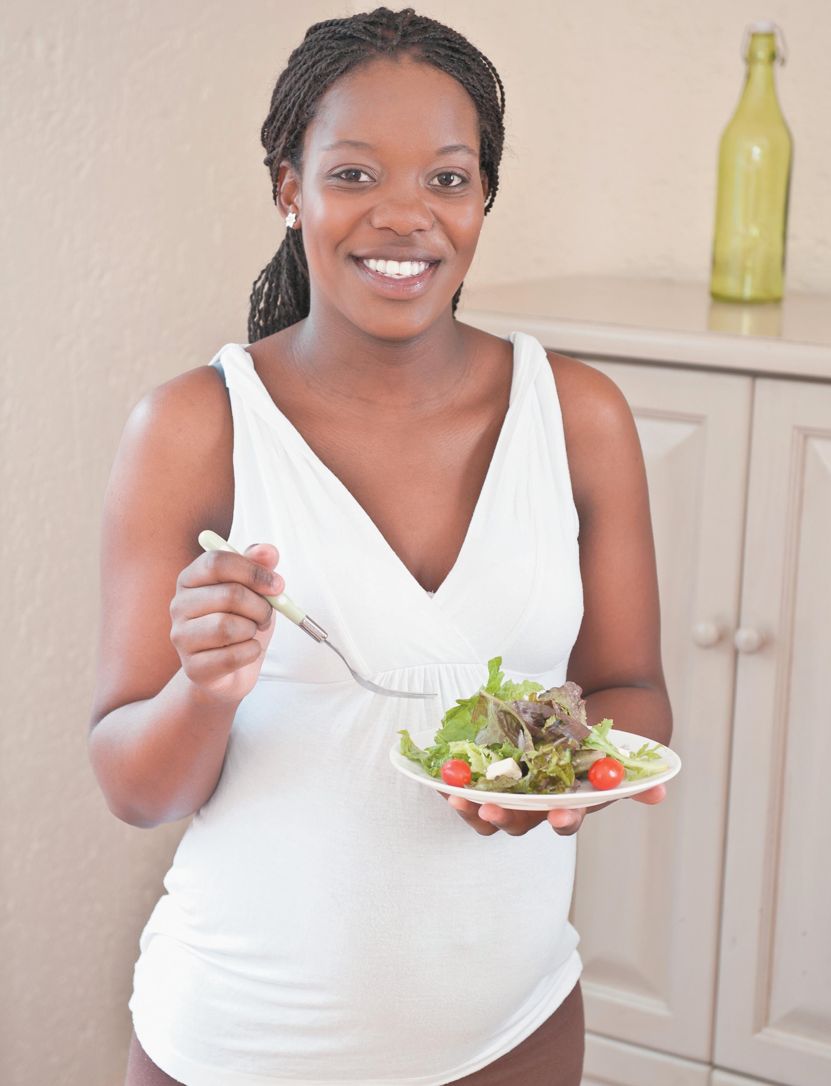 Photo of a woman smiling and eating a salad.