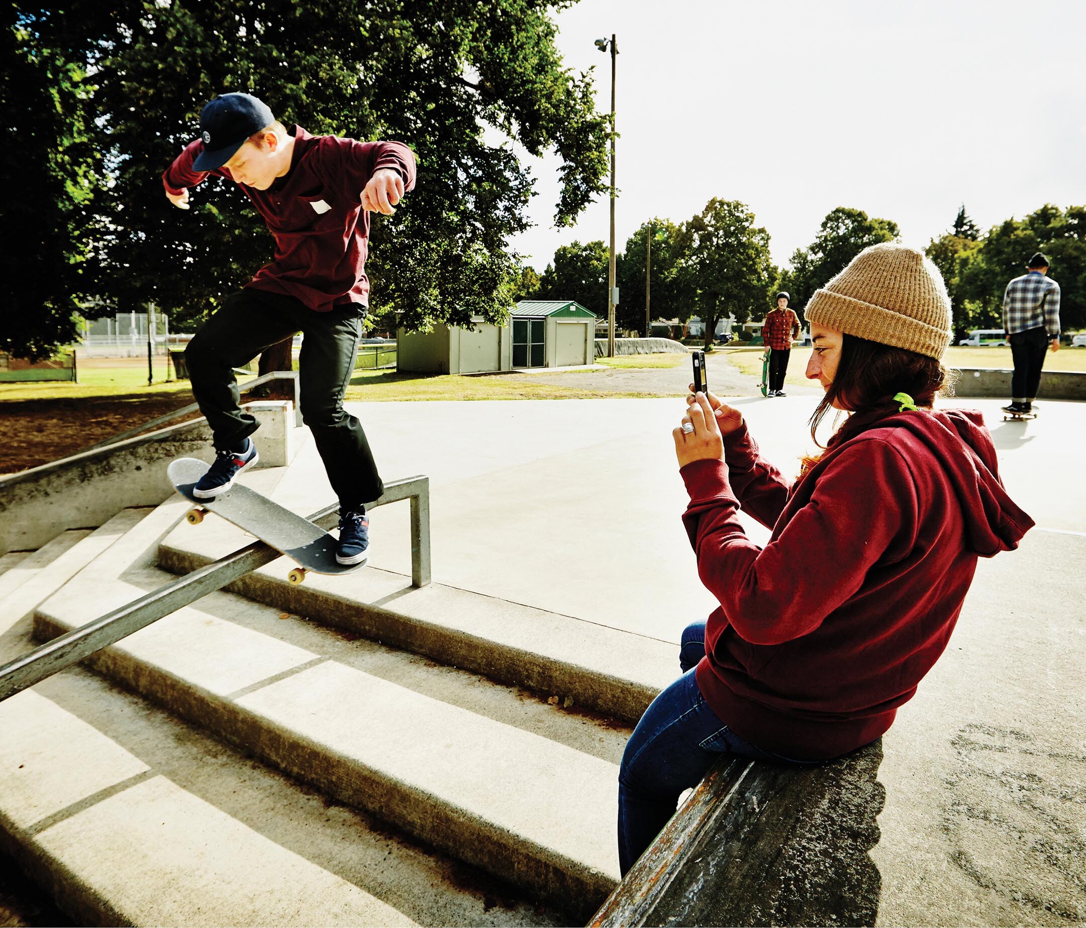A photo shows a person taking a photograph of a young boy skateboarding on a railing using a mobile.