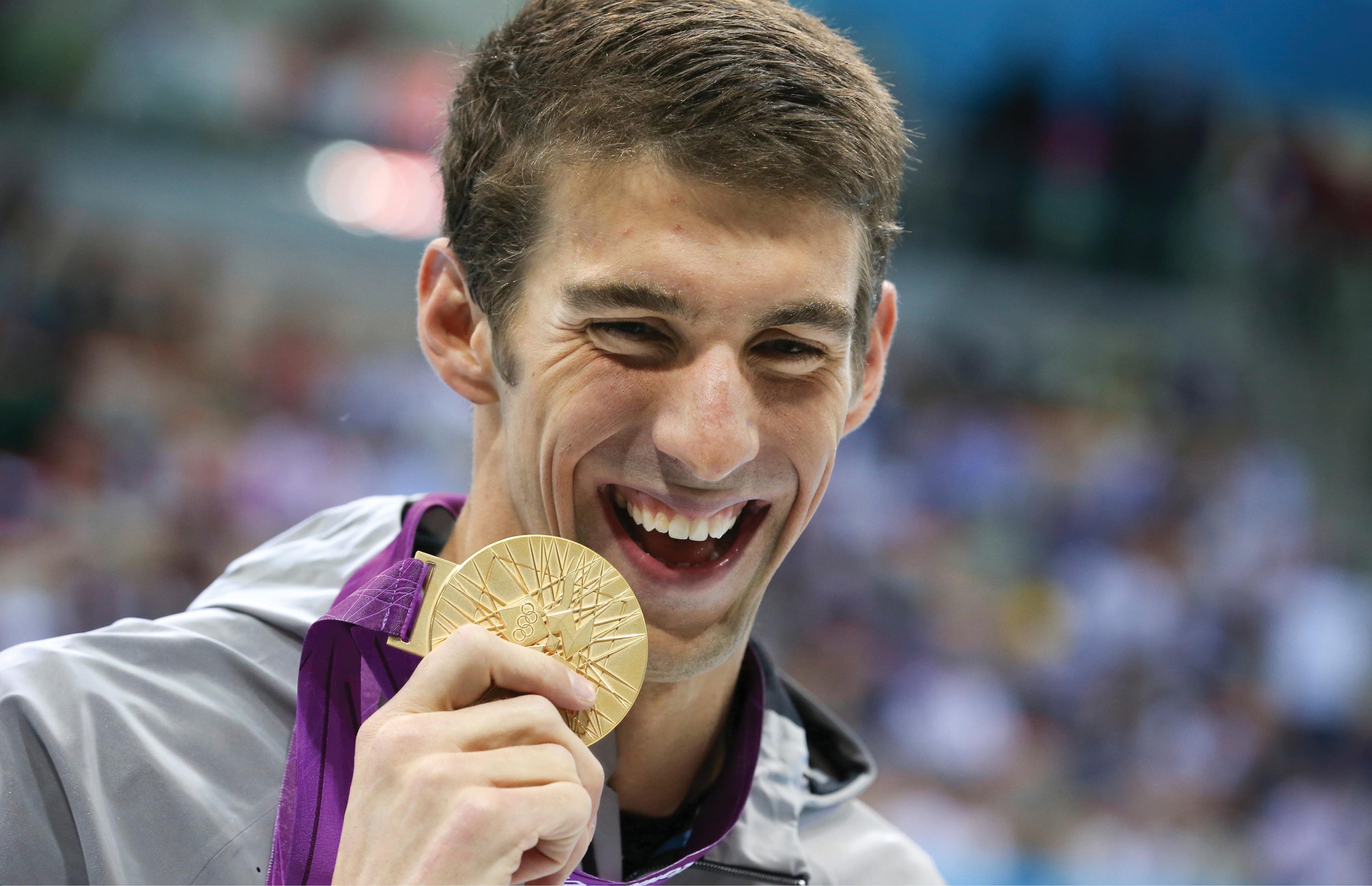 A photo of Michael Phelps holding up an Olympic trophy with a smile on his face.