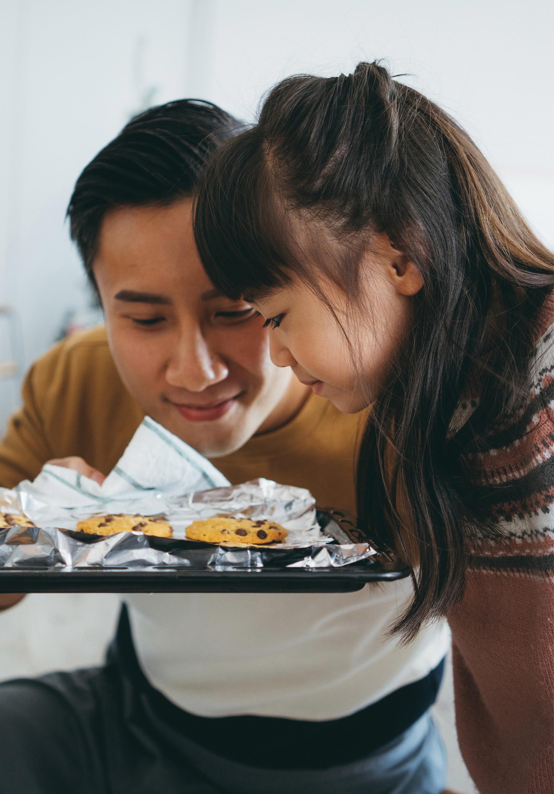 A photo of a young girl looking into a cookies tray that a man is holding.