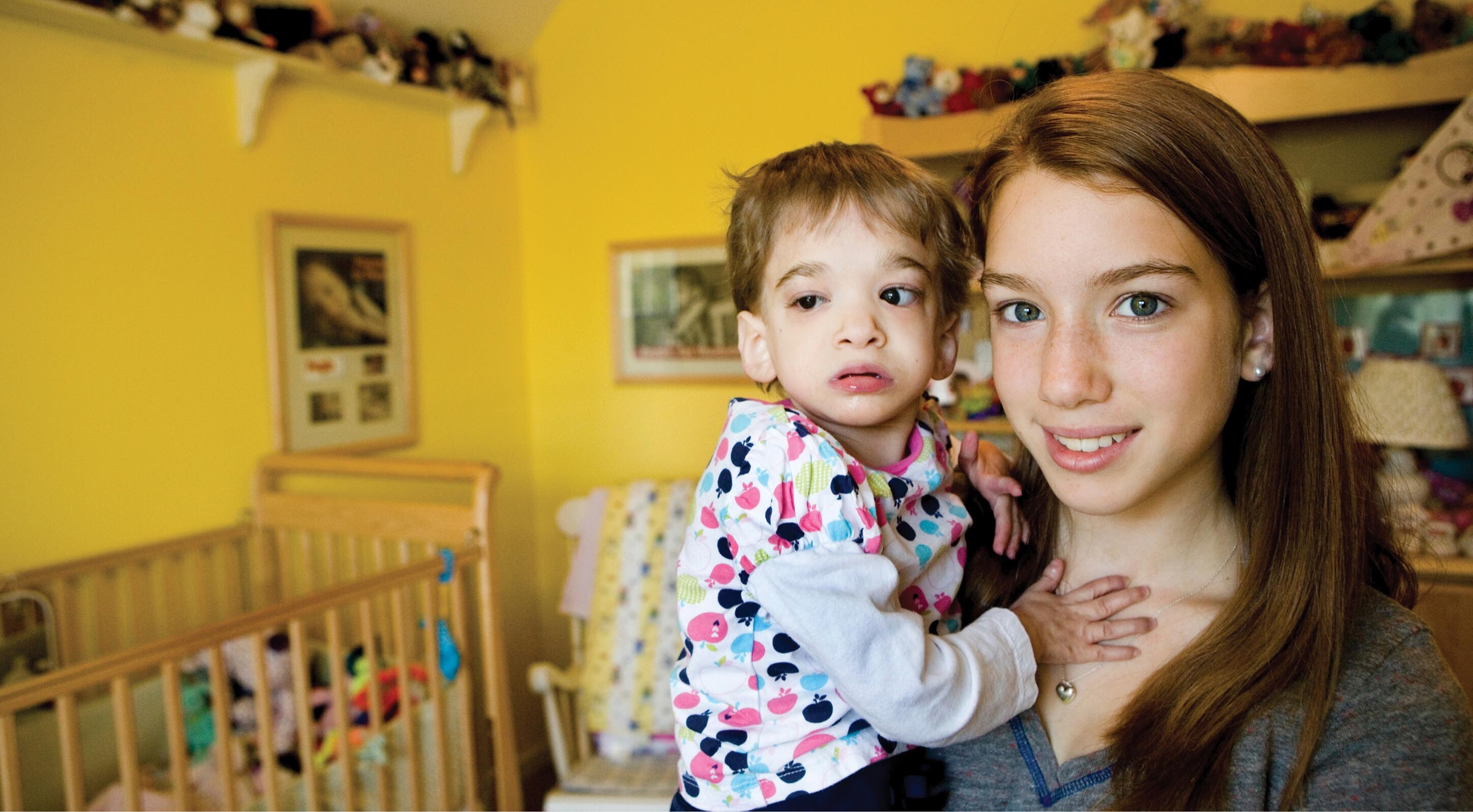 A teenage girl standing in a room holding a toddler on her hip. The toddler’s eyes are significantly different sizes.