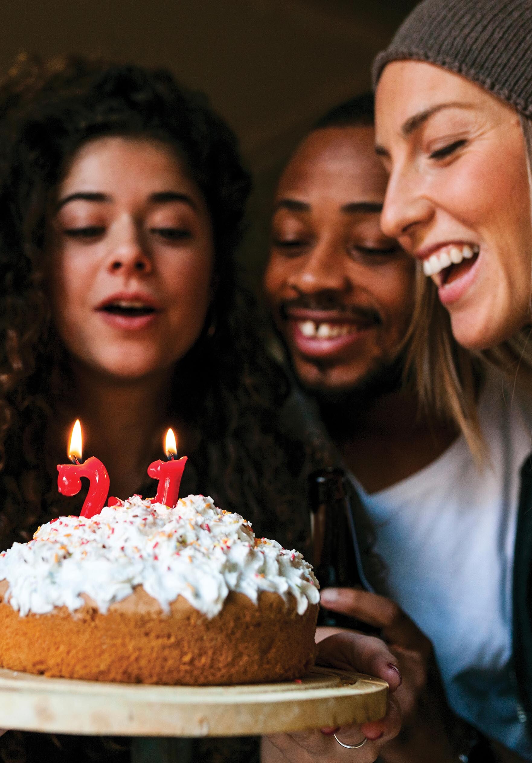 A photo of three young people with smiling faces in which one of the girls holds a cake in her hand.