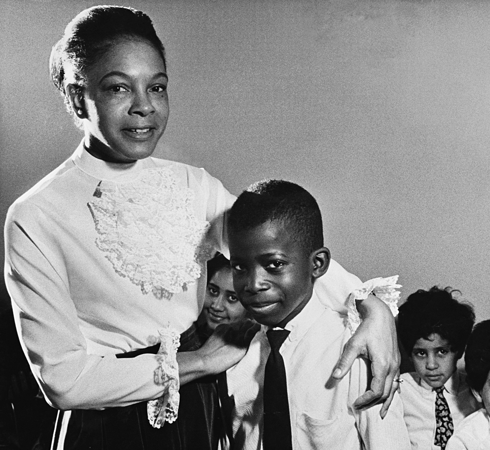 A photo shows African American Dr. Mamie Phipps Clark with her arm around a boy and surrounded by other children.