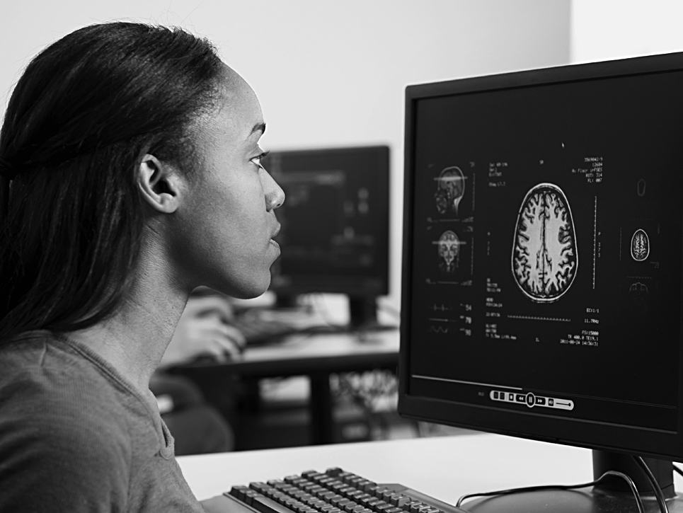 A photo shows a woman looking at a desktop computer screen which displays a scanned image of a brain.