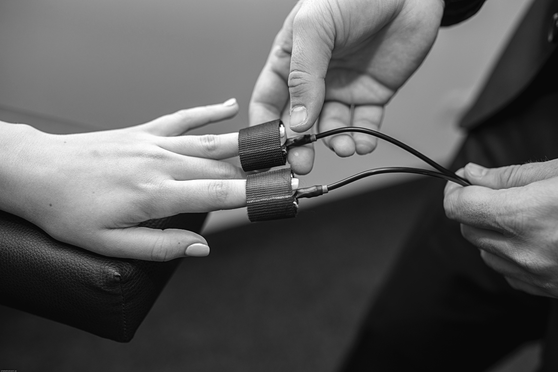 A photo shows electrodes of a lie detector being attached to two fingers of a person.
