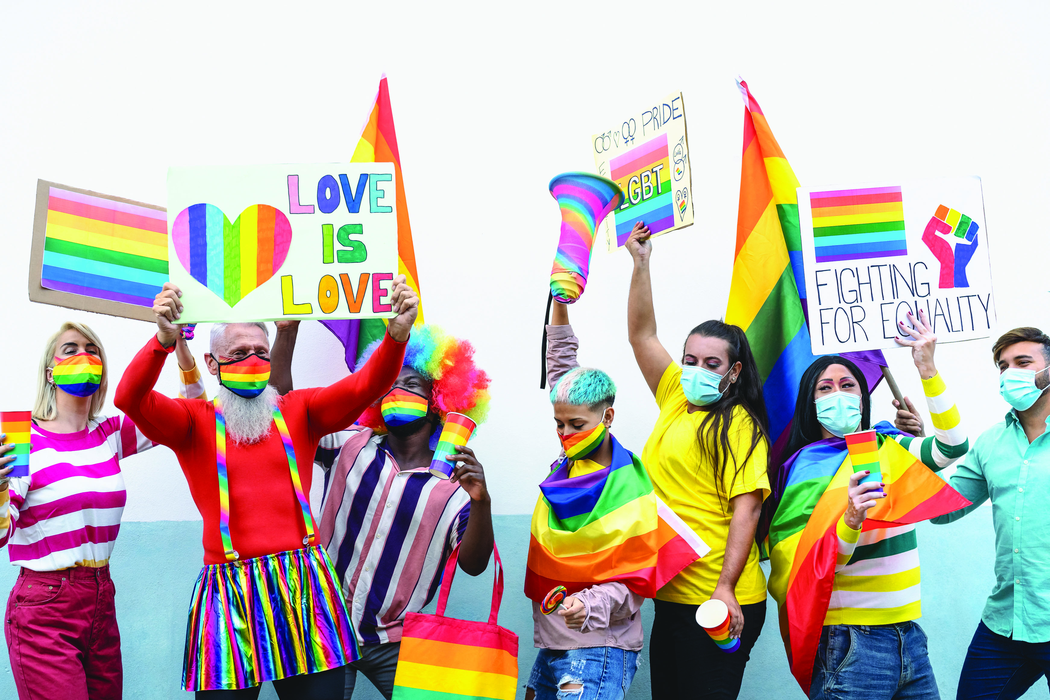 A photo shows a group of people in rainbow colored clothing, with rainbow signs, flags and masks.