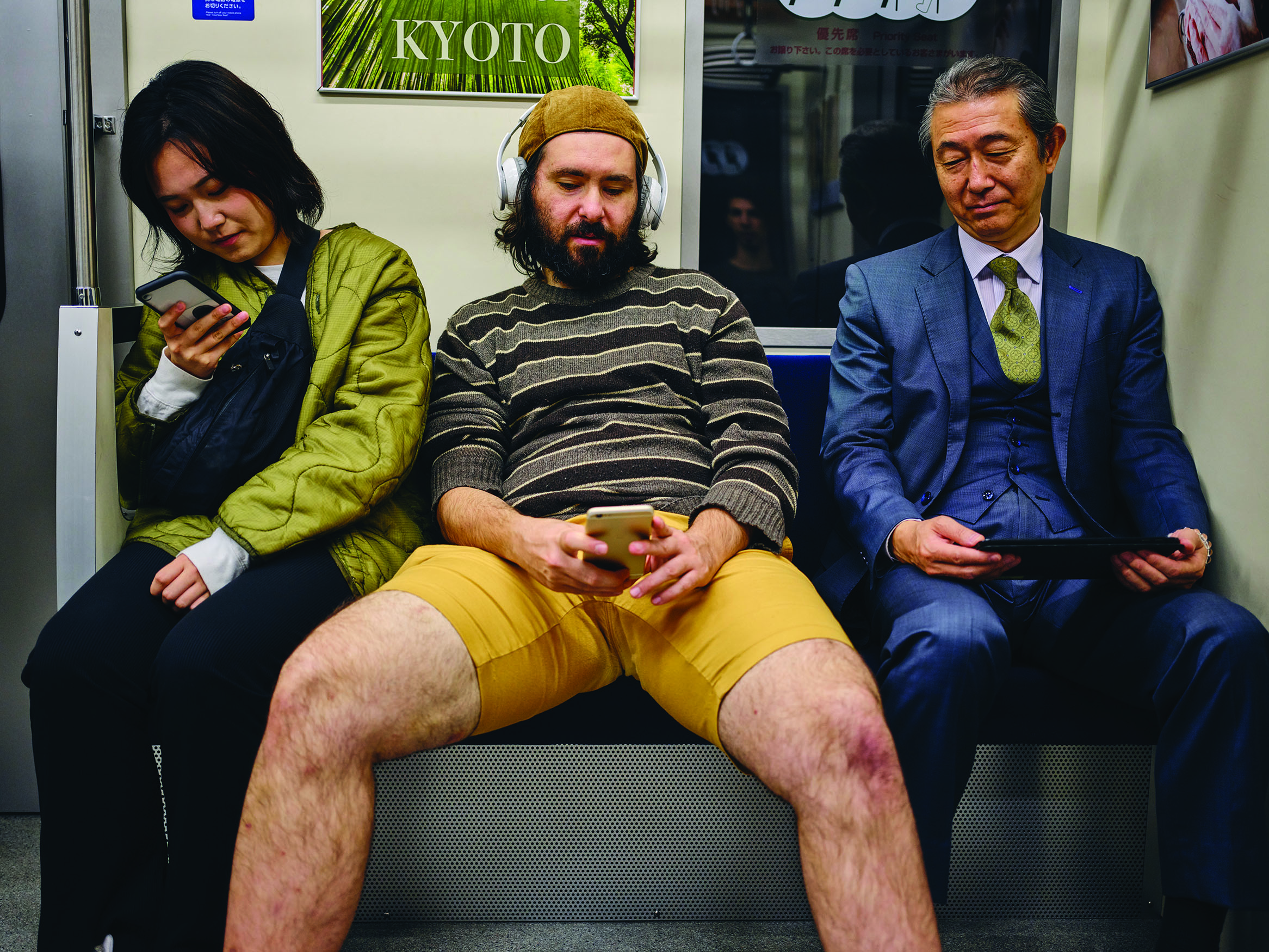 A photo shows a man on a subway sitting slouched back with his legs spread open between two other passengers.