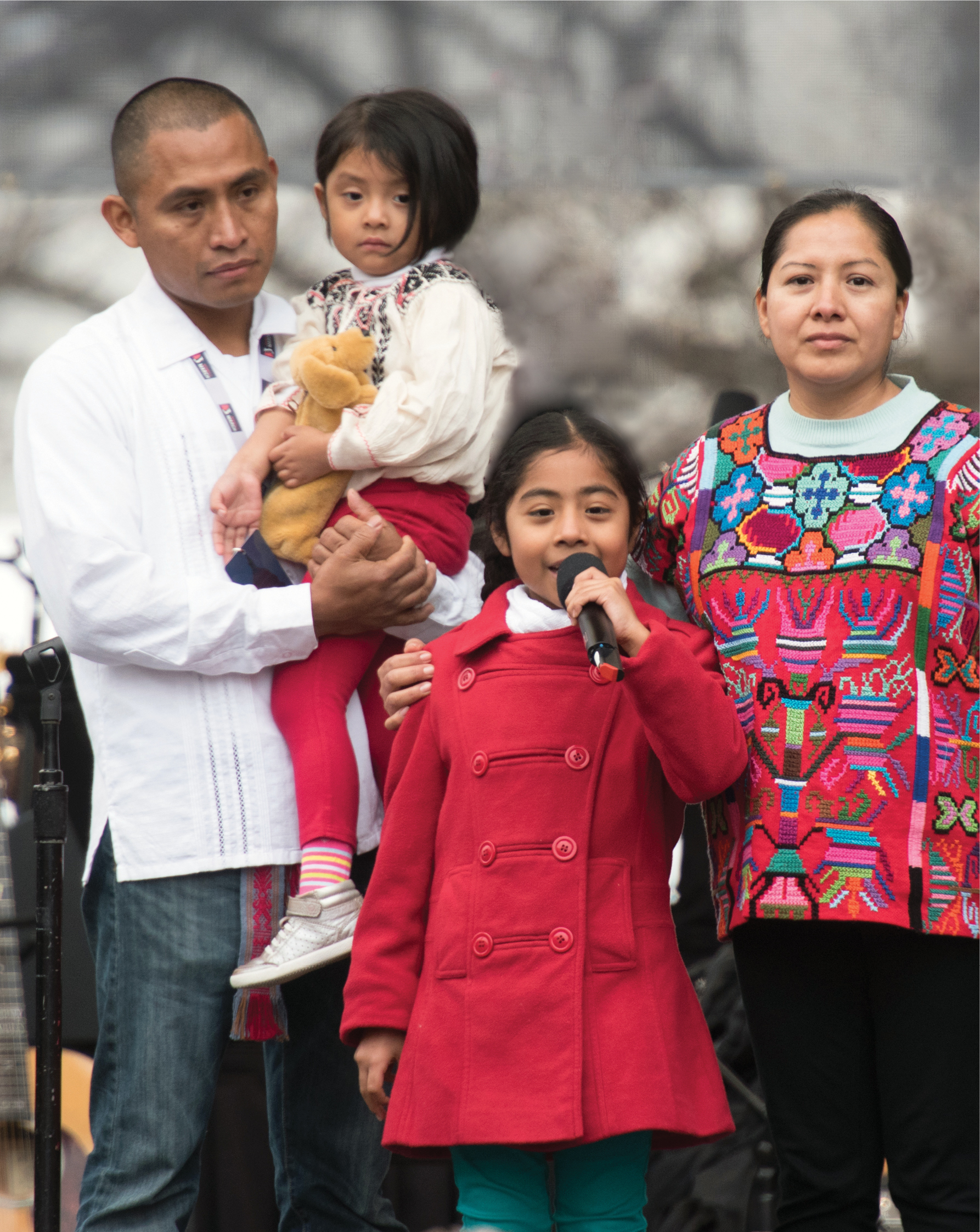 A photo shows a family of four on a stage while a young girl speaks into a microphone.
