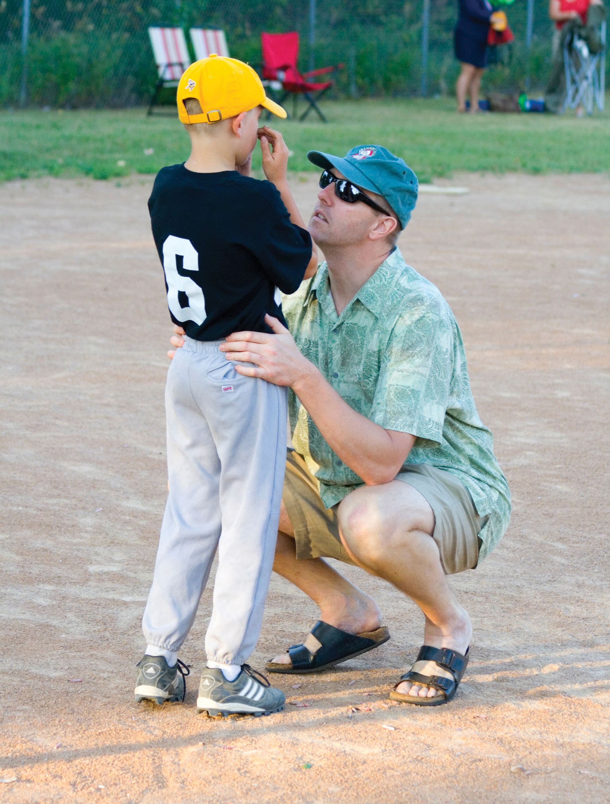 A photo shows a father on a baseball field kneeling to comfort his son, dressed in his baseball uniform, who is crying.