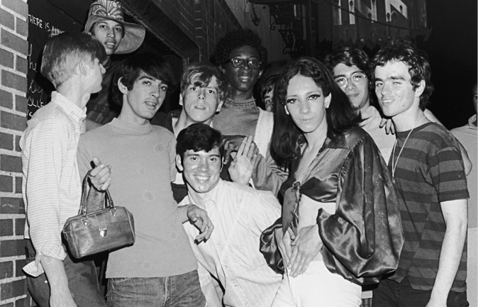 A black and white photo shows a group of young people posing in front of the Stonewall Inn.