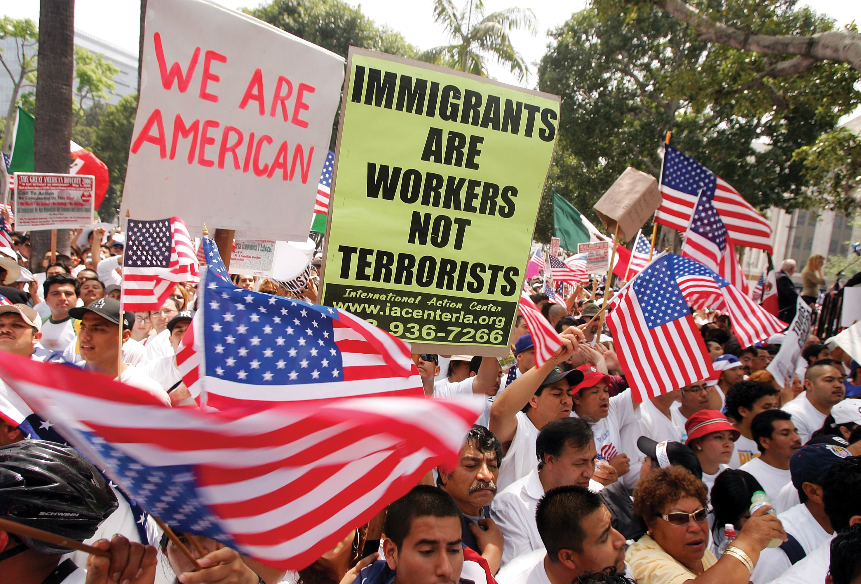 A black and white photo shows a crowd of protesters waving American flags and holding signs in favor of immigration.