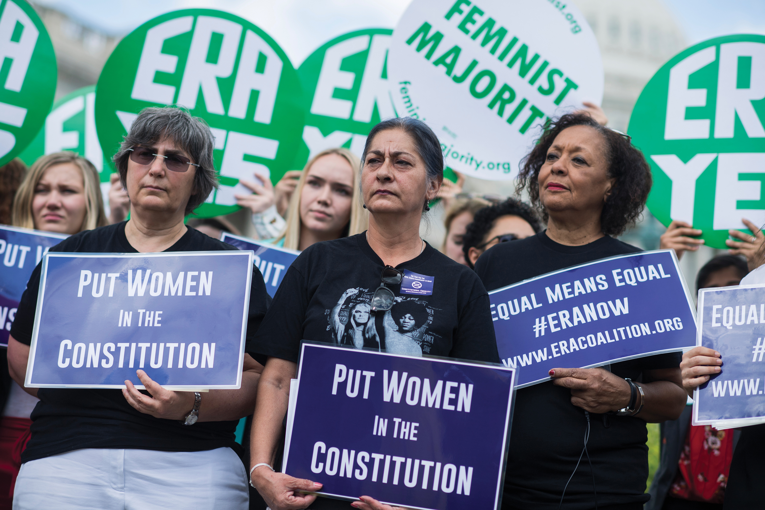 A photo shows women participating in a rally holding signs that say “put women in the constitution”