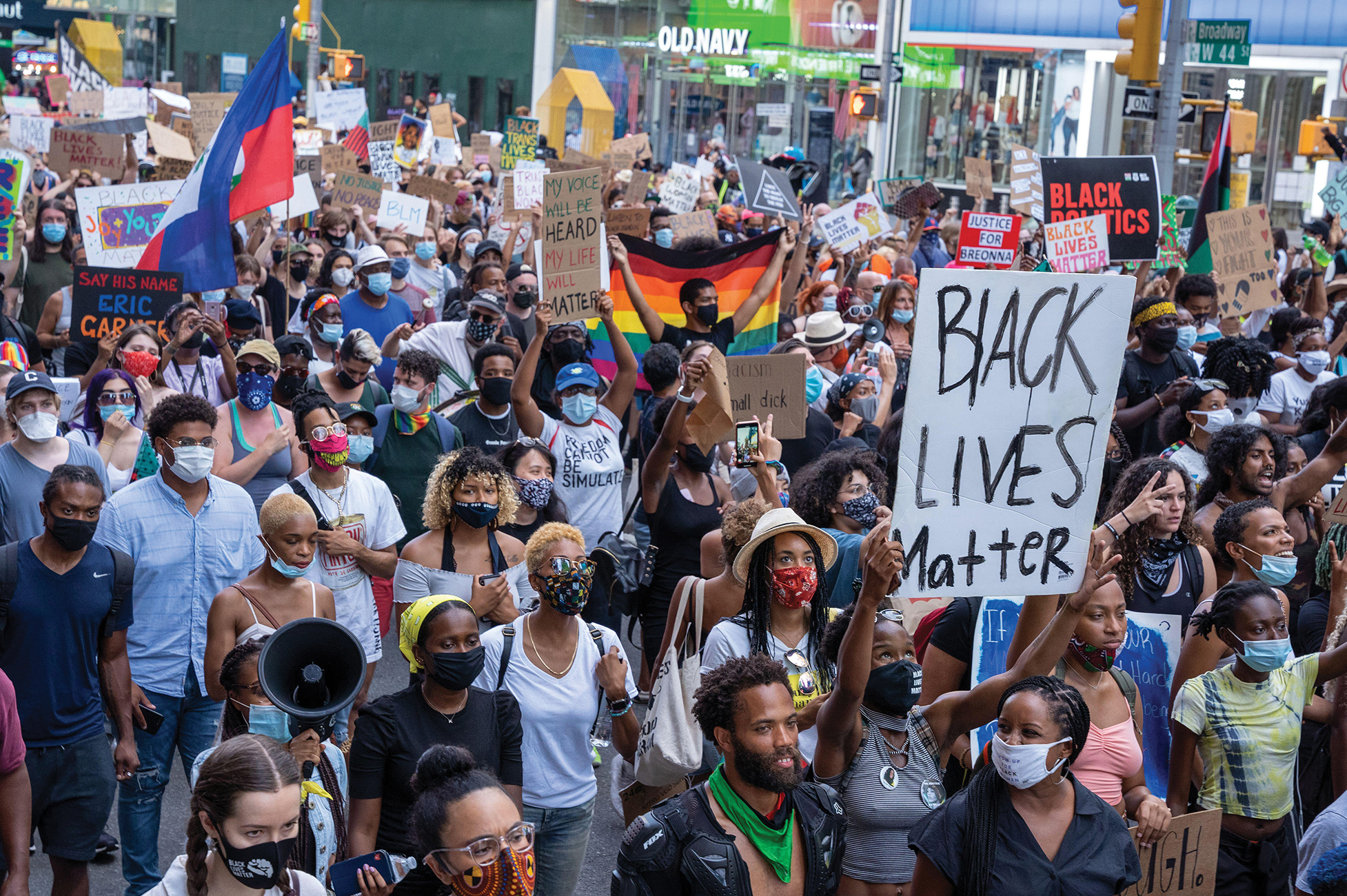 A photo shows masked and unmasked protestors at a protest in 2020, some holding signs that read “Black Lives Matter.”