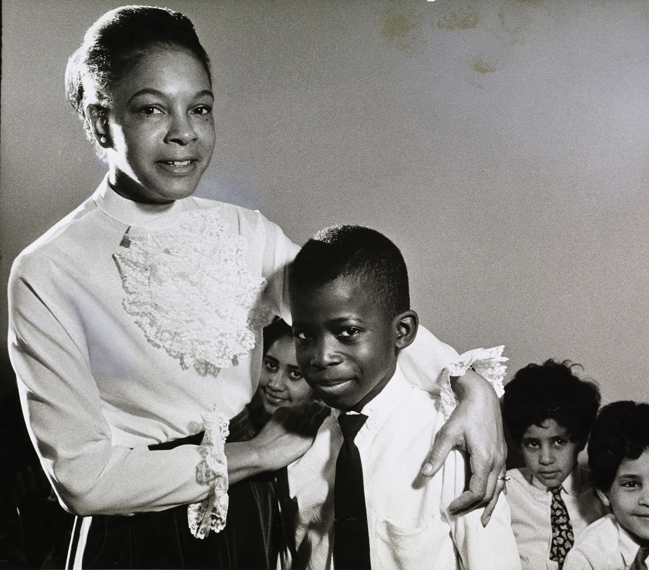 A photo shows African American Dr. Mamie Phipps Clark with her arm around a boy and surrounded by other children.