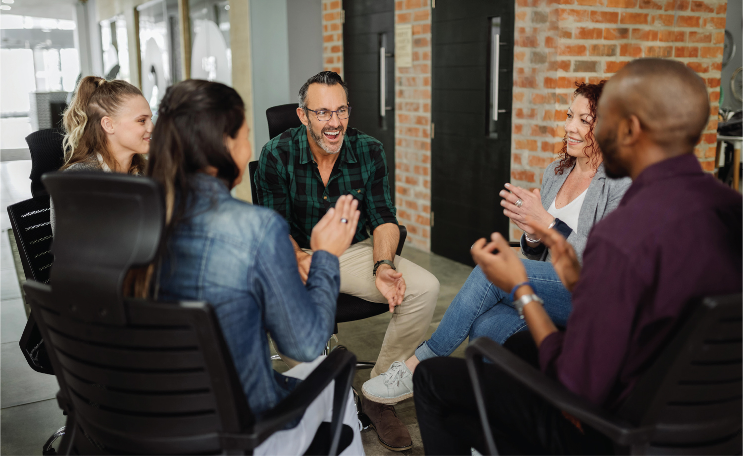 A photo shows five adults seated in chairs arranged in a circle, interacting and smiling.