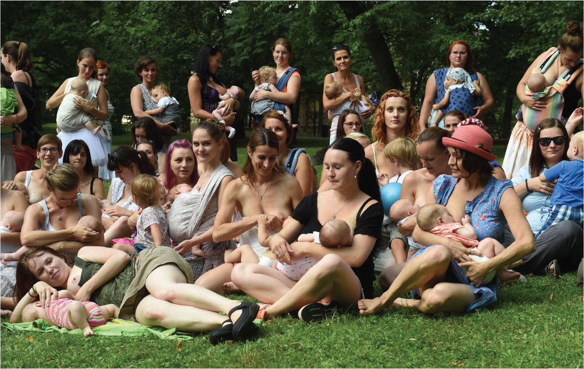 A photo shows a large group of women breastfeeding on a lawn in a public outdoor space.