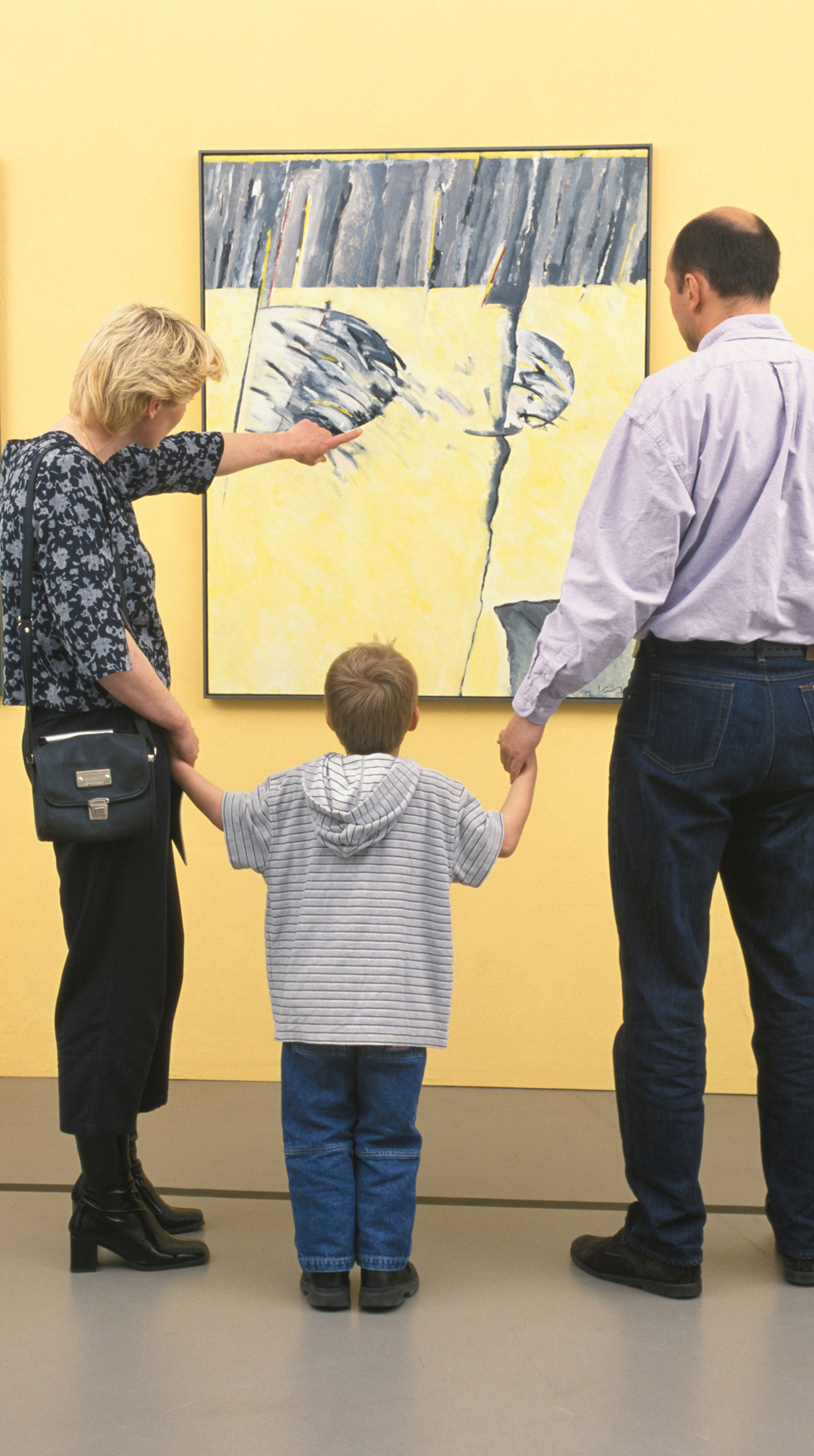 Chapter 7 Opener. A man and woman stand holding the hands of a boy between them. They are looking at a piece of art hung on the wall.