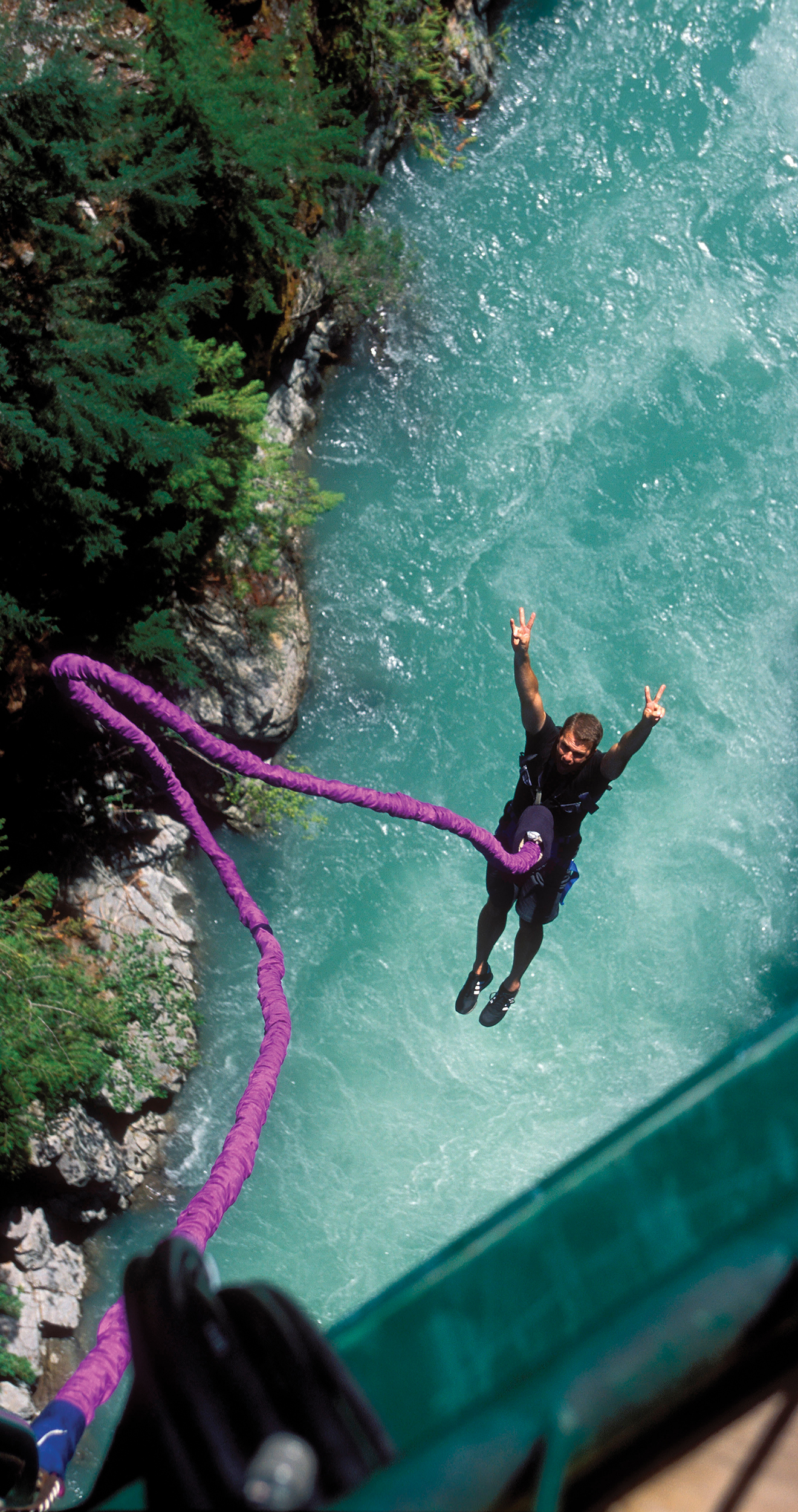 A photo shows a top down view of a man bungee jumping from a bridge with a river below.