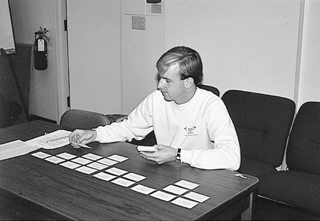 A black and white photo shows a man sitting at a table arranging cards in front of him.