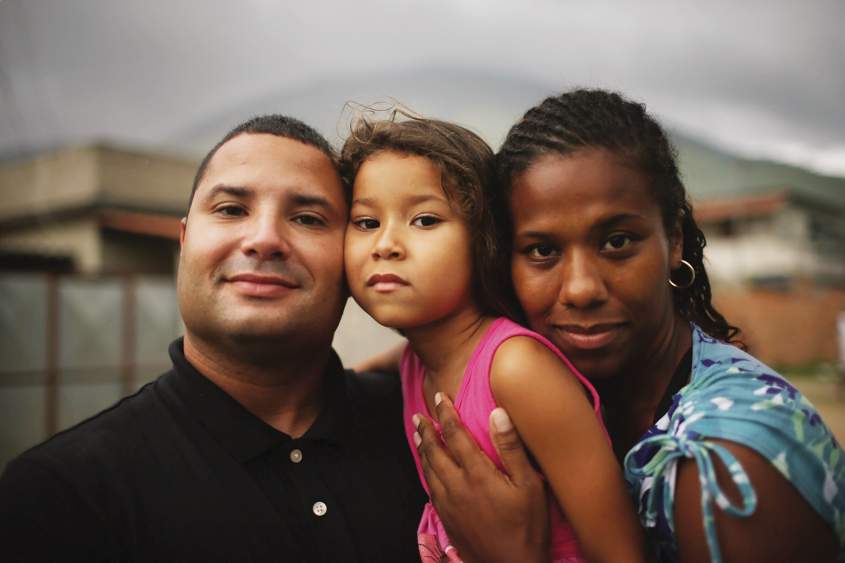 In a photograph, a Brazilian family of three shares an embrace.