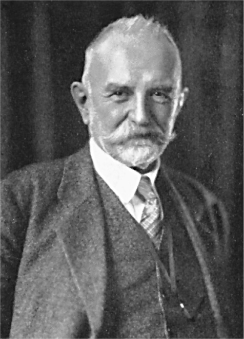 A black-and-white portrait of a white man with a gray mustache and beard wearing a suit.