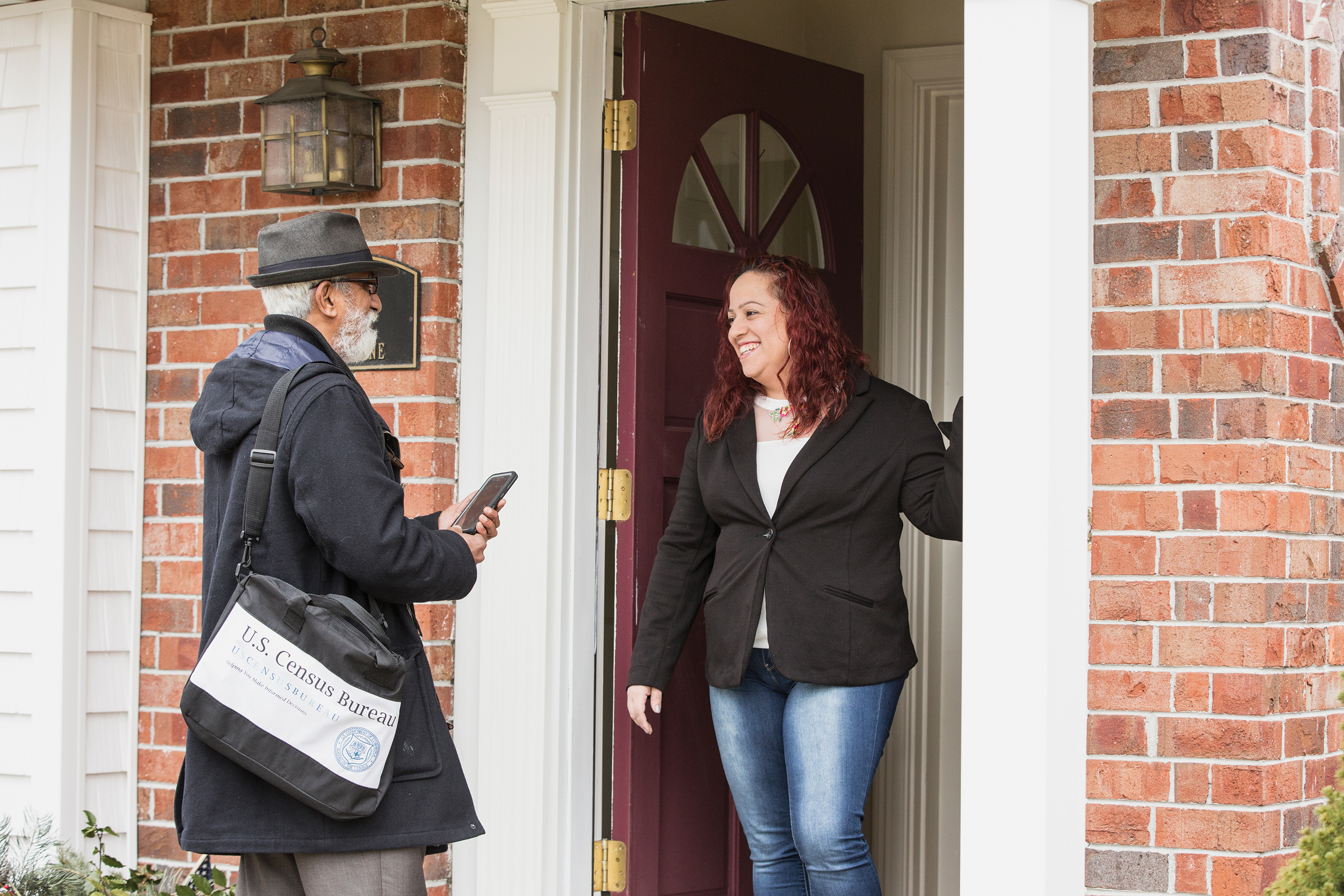 An older man stands near the entrance of a house and talks to a woman who has the door to her home open behind her.