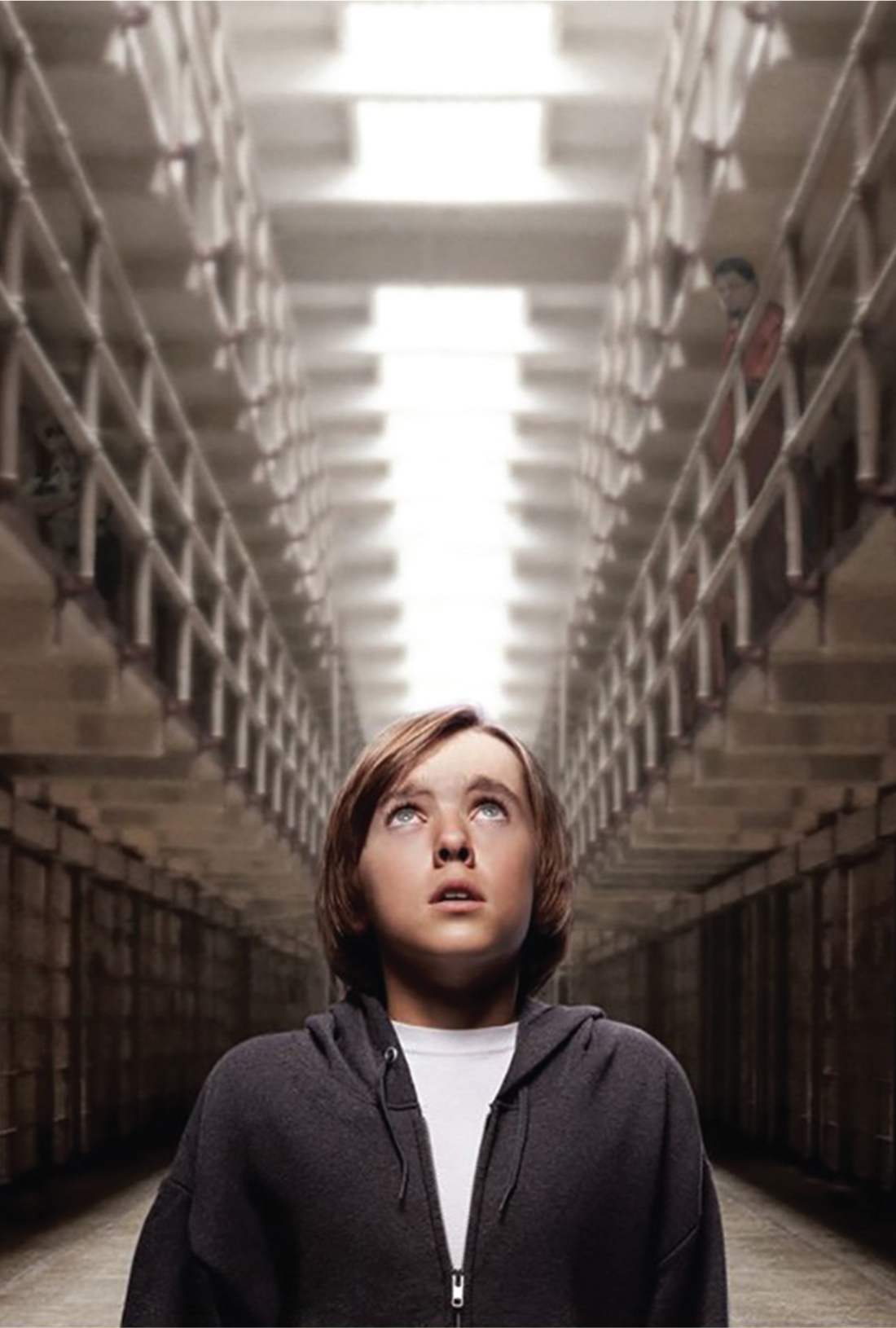 A boy looking up while standing in the center of a prison hall.