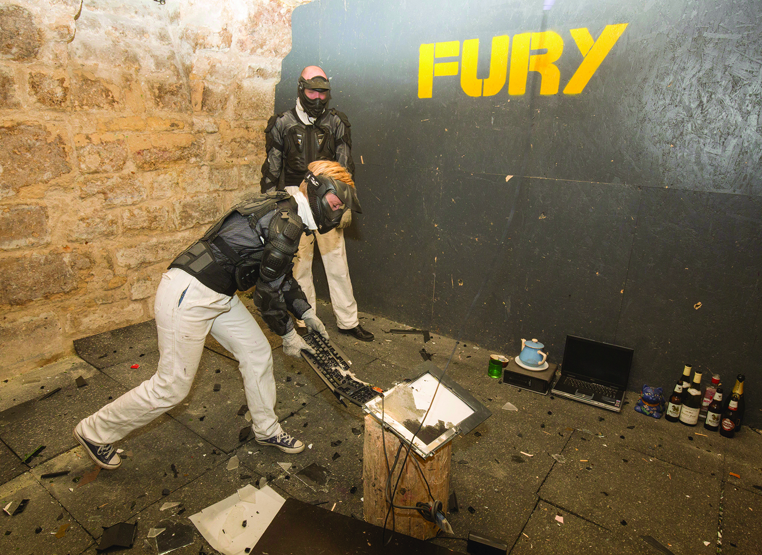 A man with a mask smashing a keyboard against a log while another man in the same mask watches.