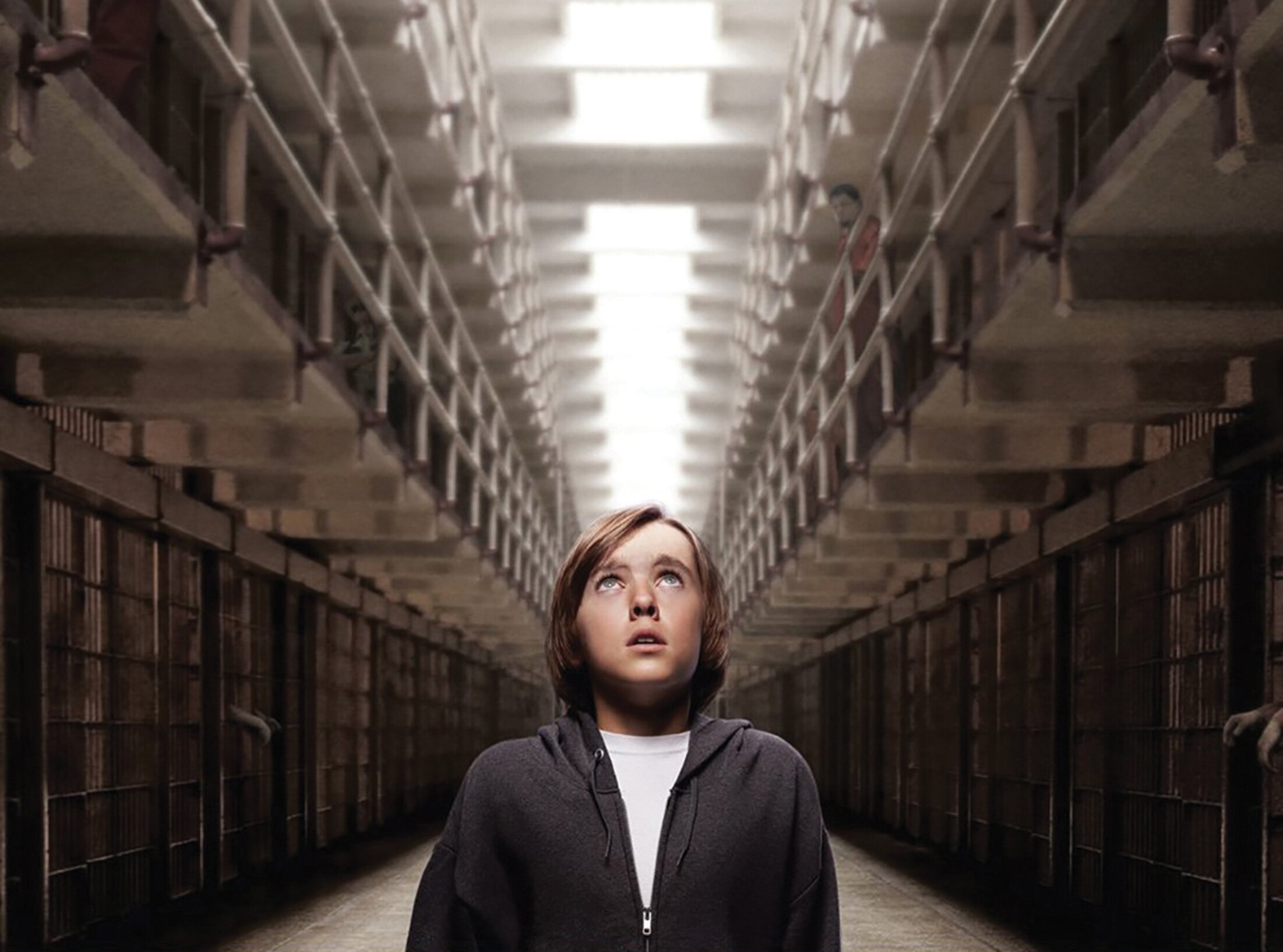 Two images show a boy looking up while standing in the center of a prison hall and a man sitting on the edge of his seat with perfect posture in a classroom. His arms rest on his knees, and his eyes are closed.
