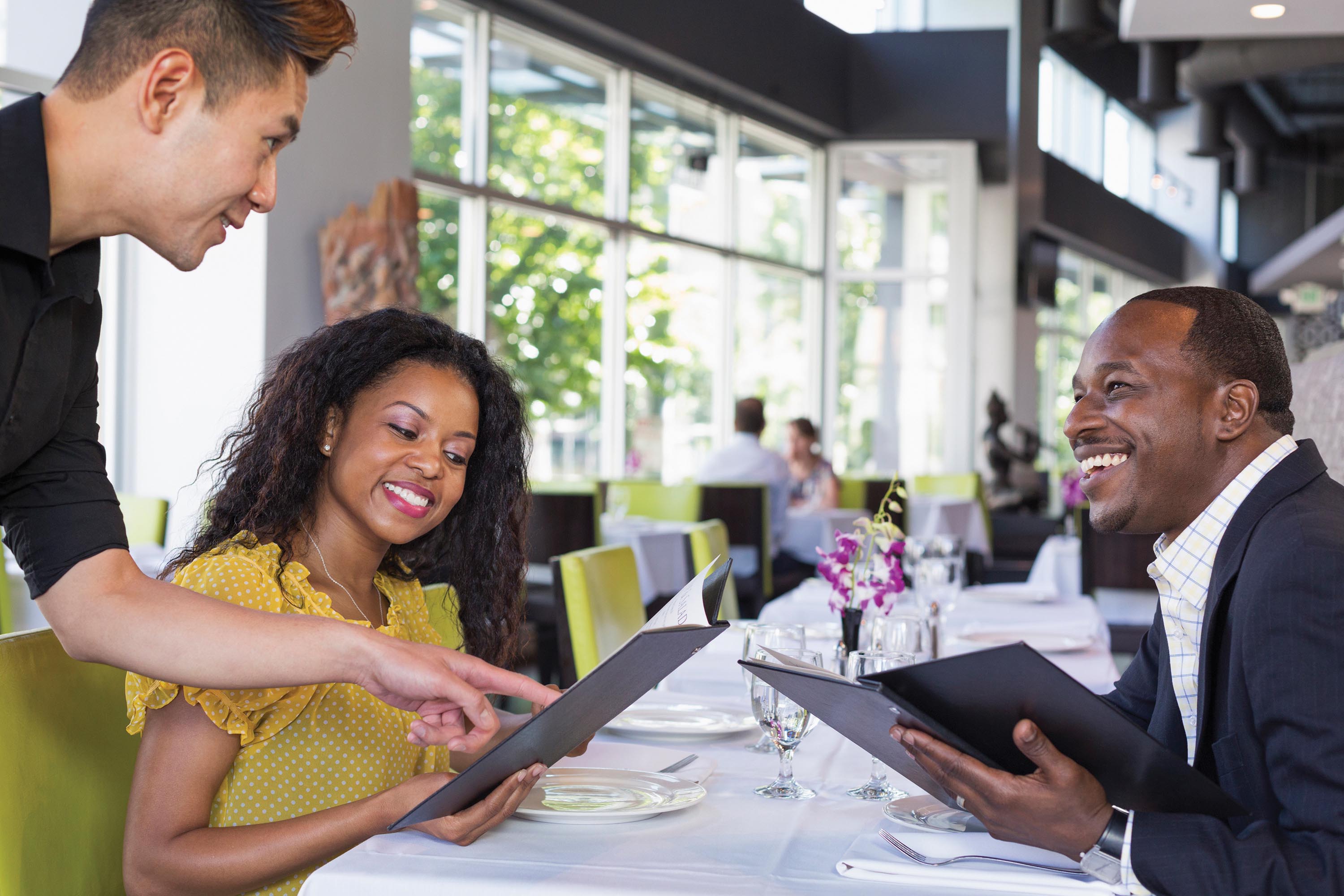 A fancy restaurant shows a waiter taking the order from a man and a woman holding menus.