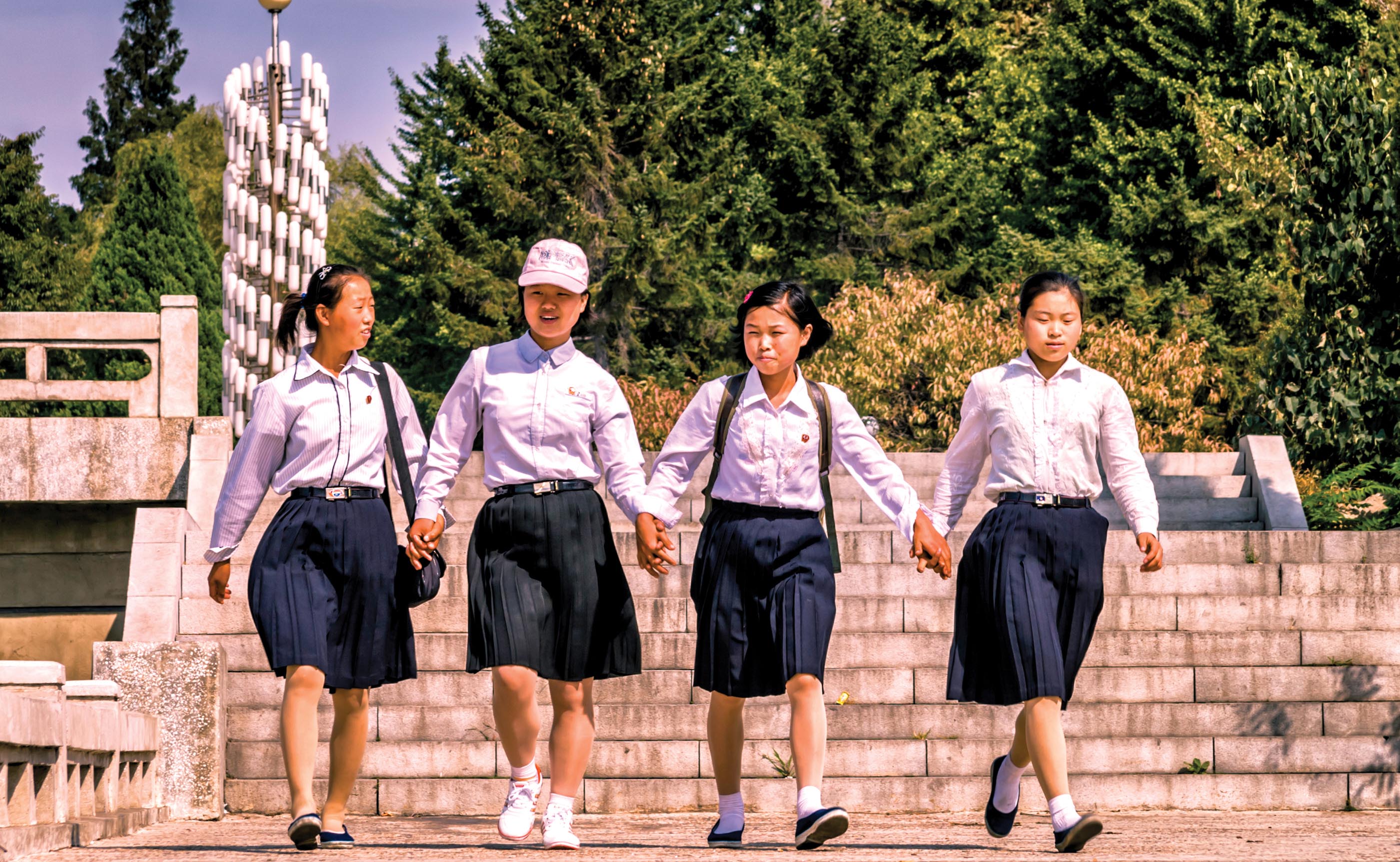 Four girls wearing uniform hold each other’s hands as they walk together.