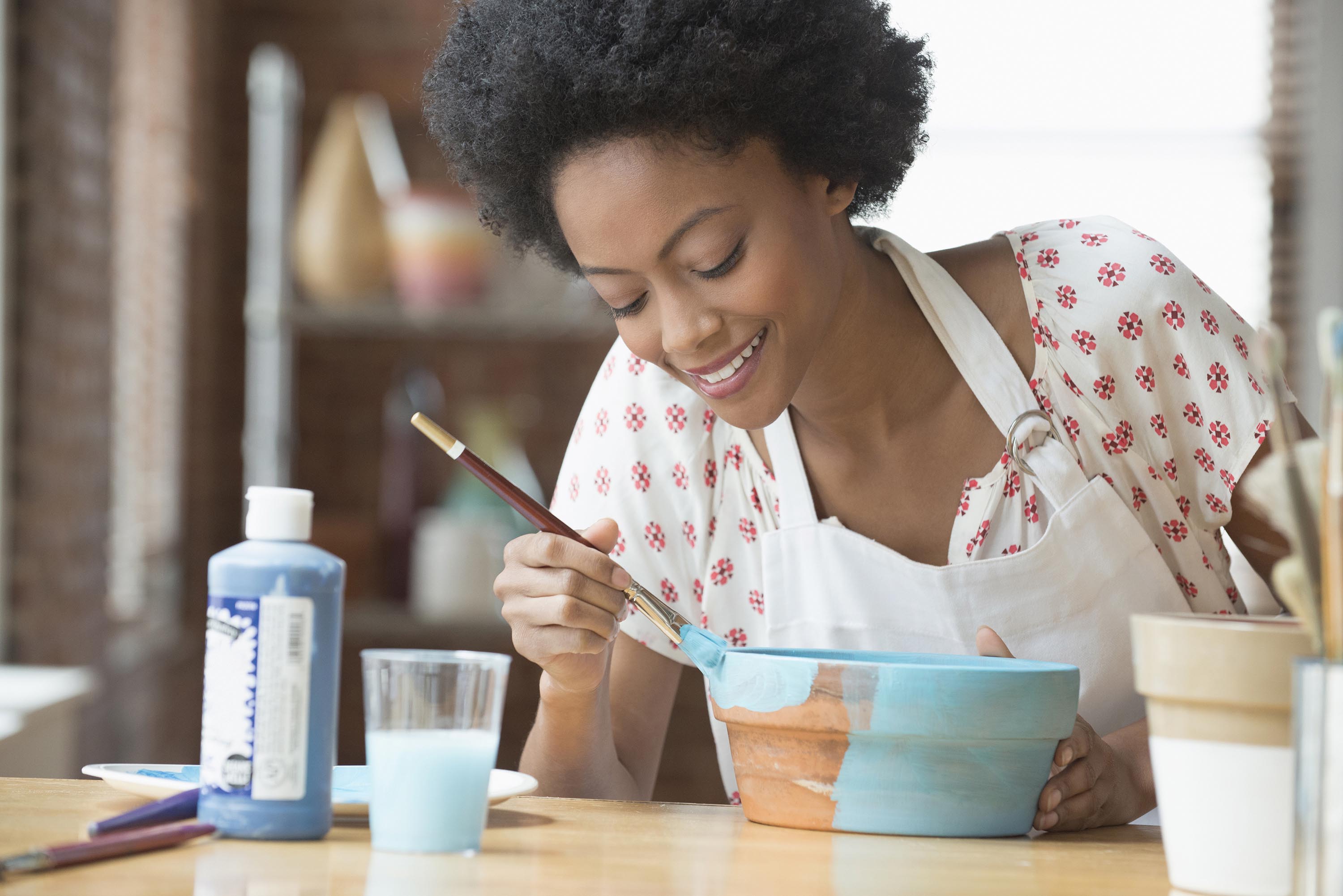 A lady wearing an apron paints a bowl.