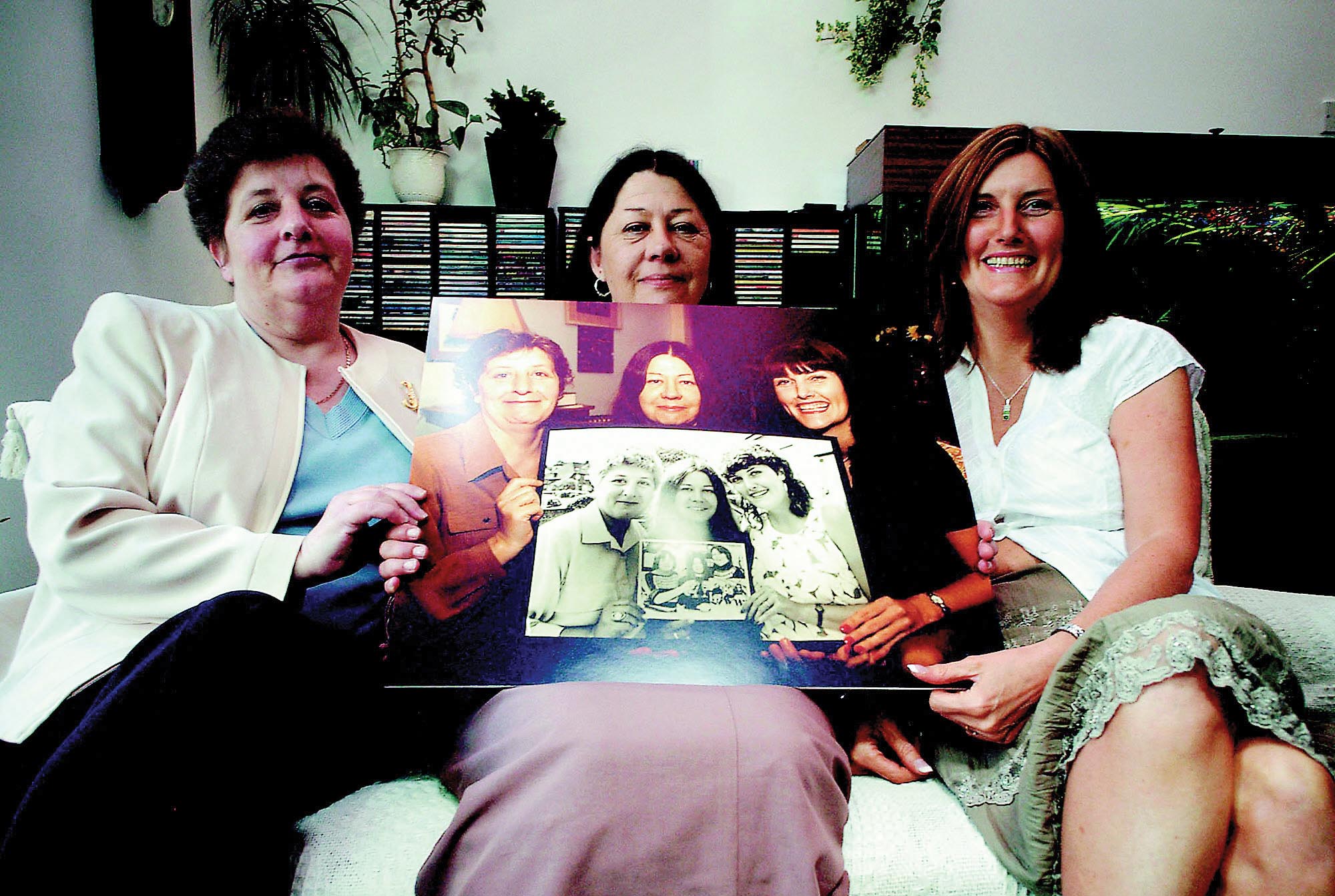 Jackie, Sue, and Lynn sitting on a couch, holding a photograph in their hands.