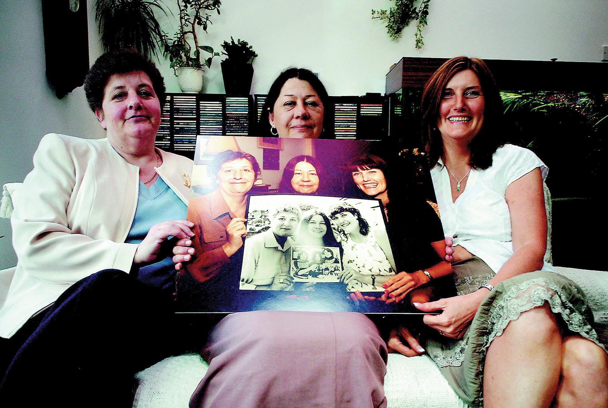 Jackie, Sue, and Lynn sitting on a couch, holding a photograph in their hands.