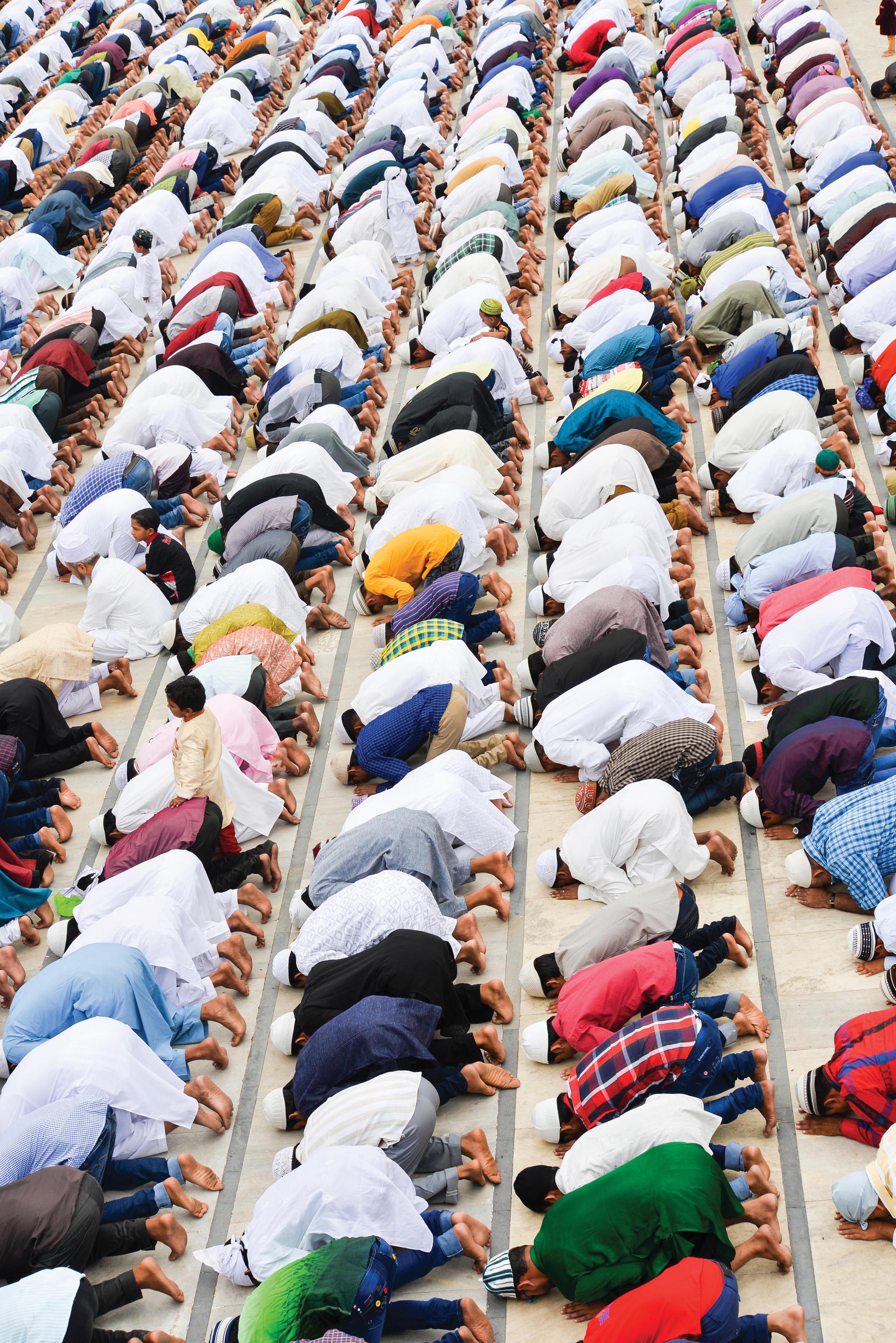 A photo shows people from the Muslim community bowing and offering prayers in a mosque.