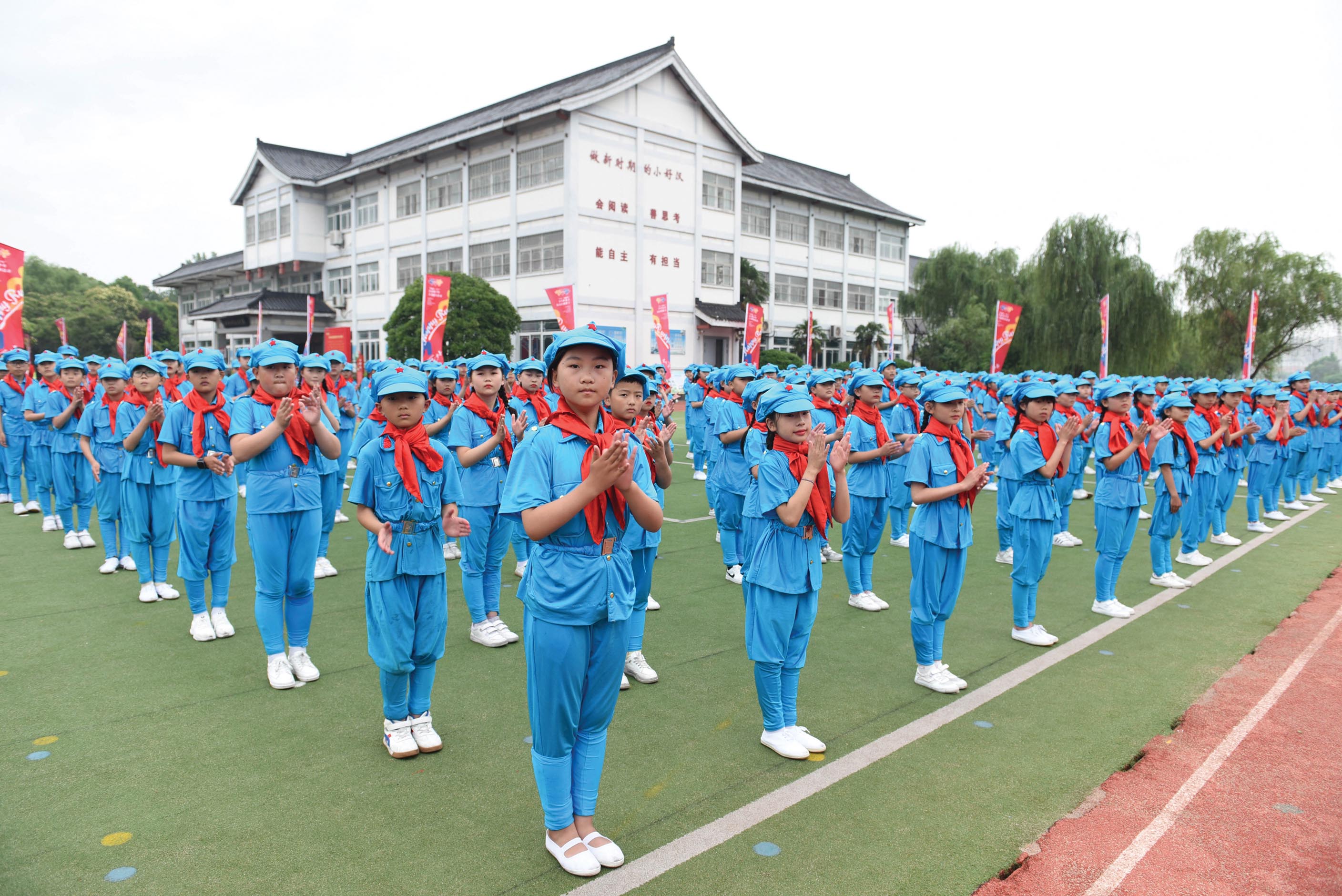 A photo of young, Asian students in school uniforms assembled in rows in an organized manner. They clap their hands.