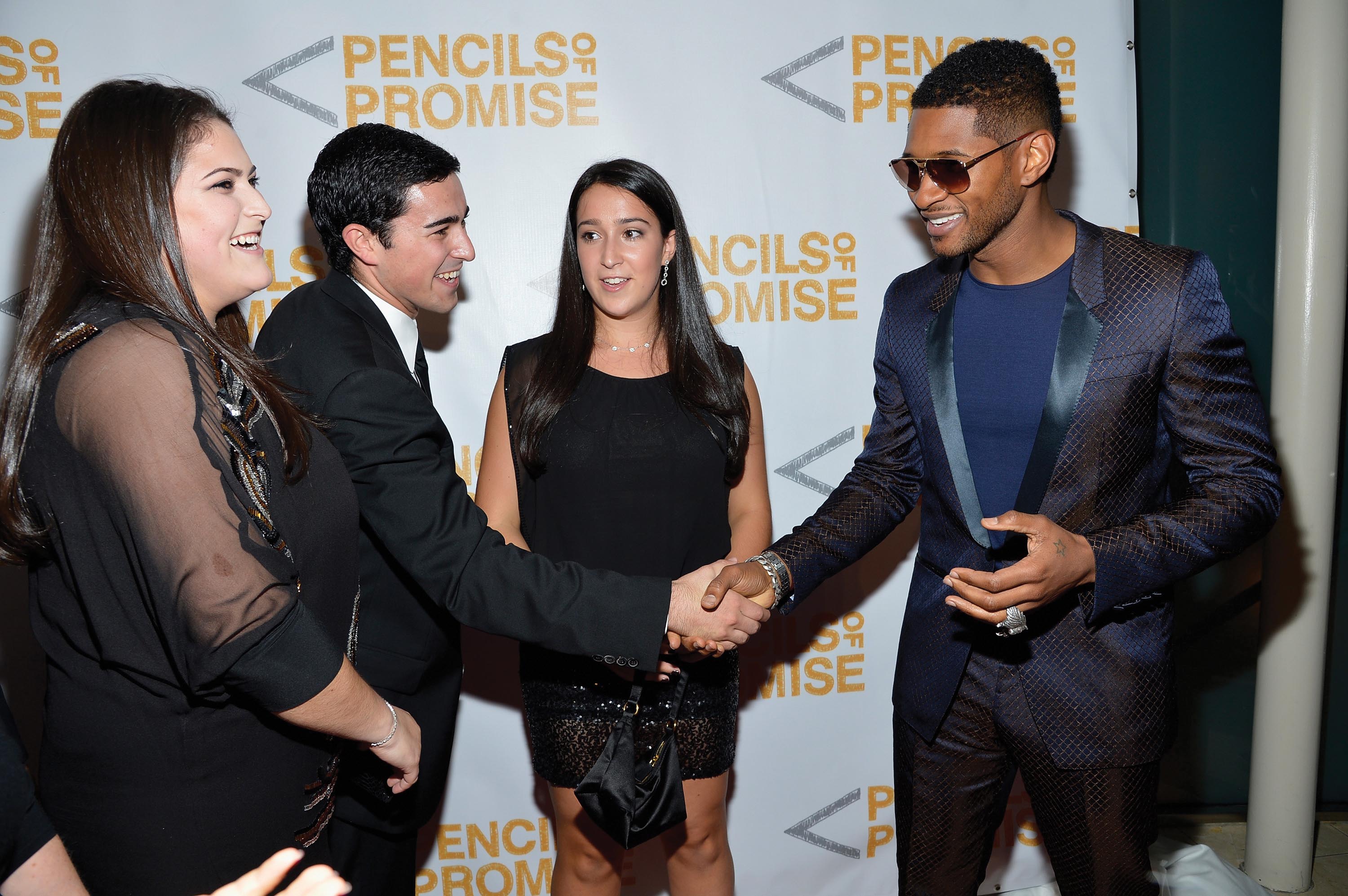 Usher smiles and shakes hands with a Pencils of Promise charity attendee while two women standing near them look at them with smiling faces.Usher smiles and shakes hands with a Pencils of Promise charity attendee while two women standing near them look at them with smiling faces.