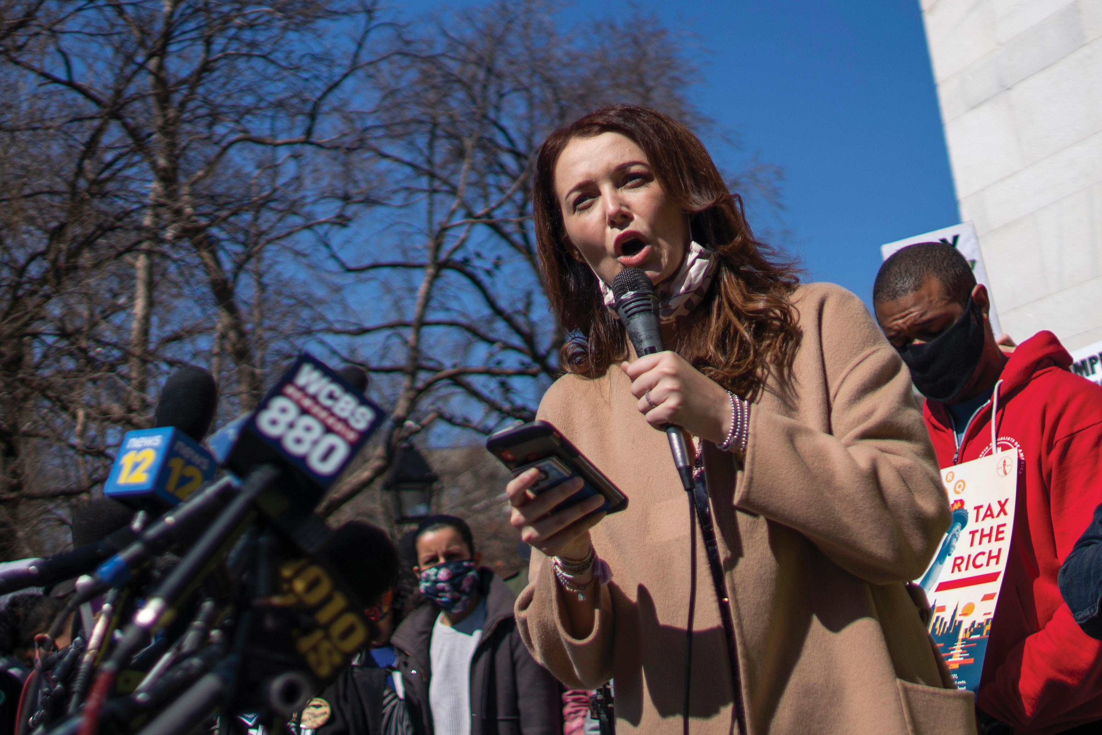 A photo of Lindsey Boylan holding a mobile in one hand and addressing the press.