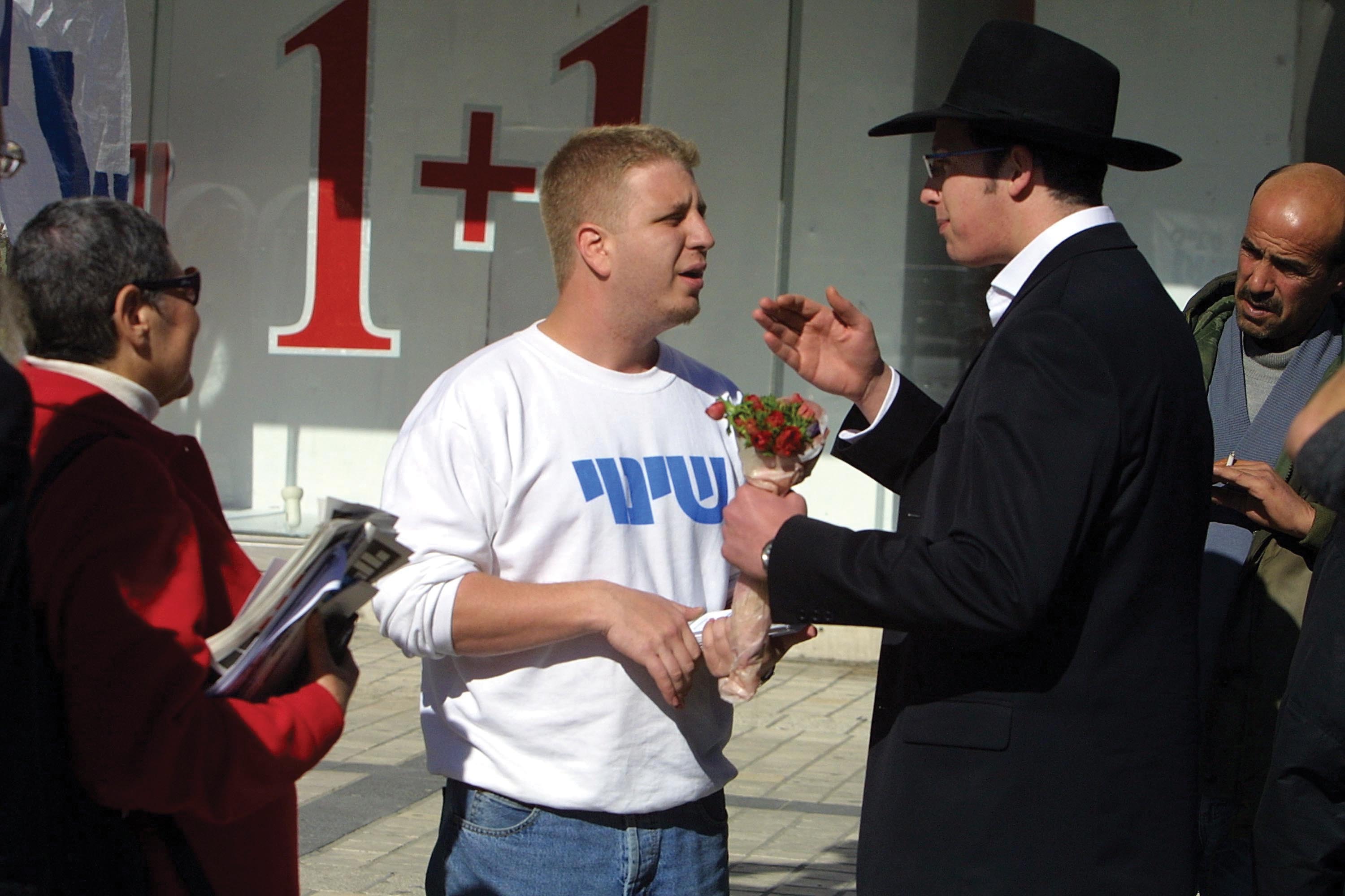 Two men face each other, discussing. One of the men wears a hat.